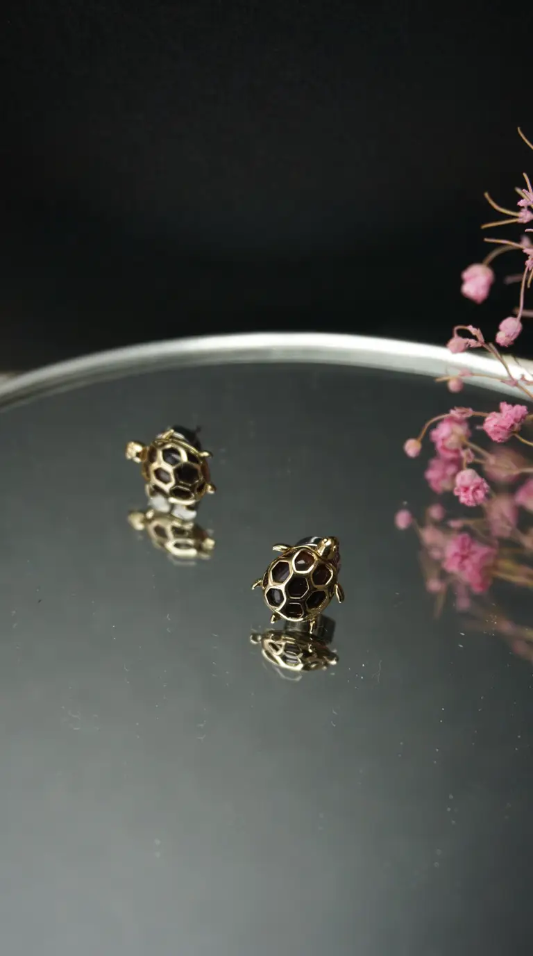 Pair of vintage gold turtle earrings with black enamel hexagonal shells, displayed on a reflective surface with pink flowers.