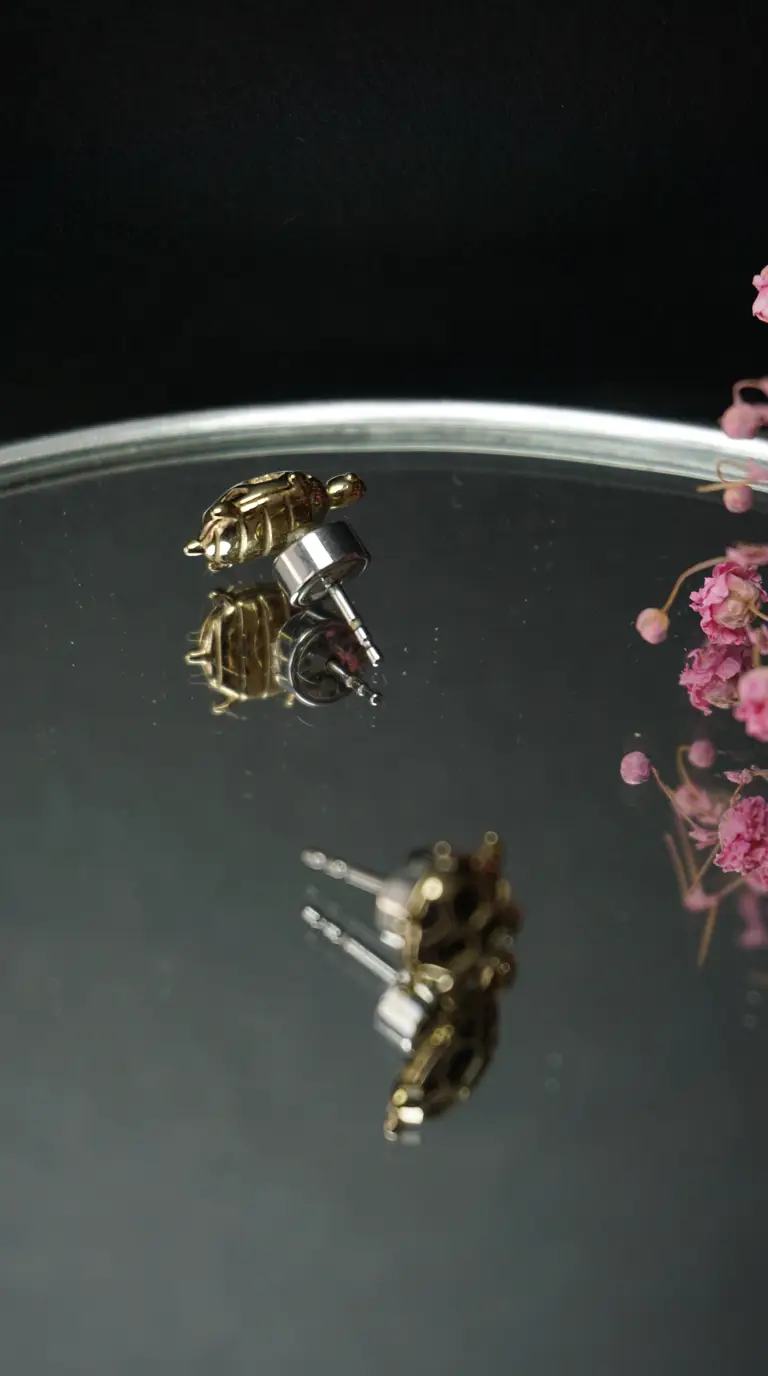Vintage gold turtle stud earrings on mirrored surface with pink flowers