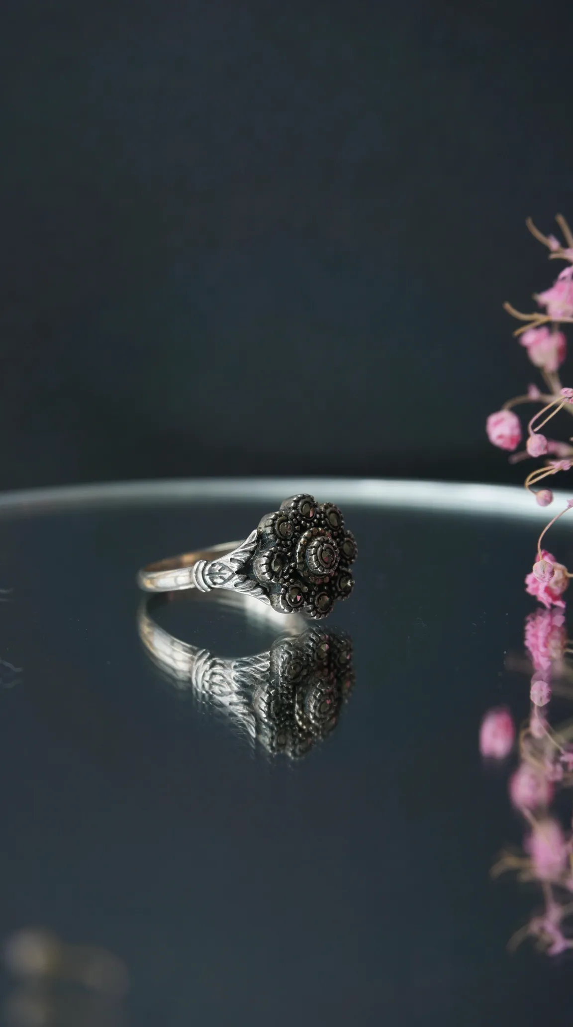 Vintage sterling silver marcasite floral cluster ring on a reflective surface