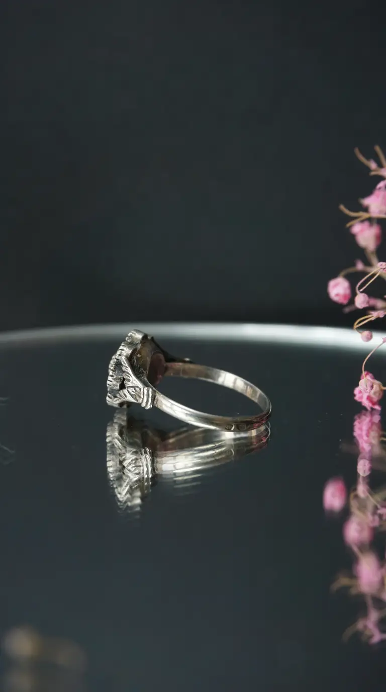 Vintage sterling silver ring with ornate details, side view on reflective surface with delicate pink flowers.