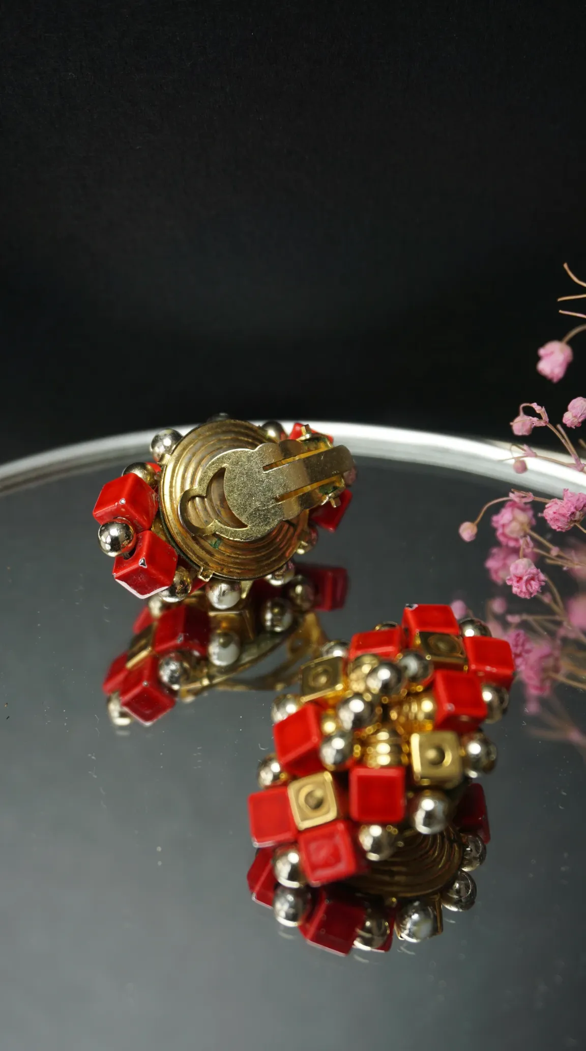Vintage gold-tone clip-on earrings with clustered red geometric cubes and silver beads, reflected on a polished surface.