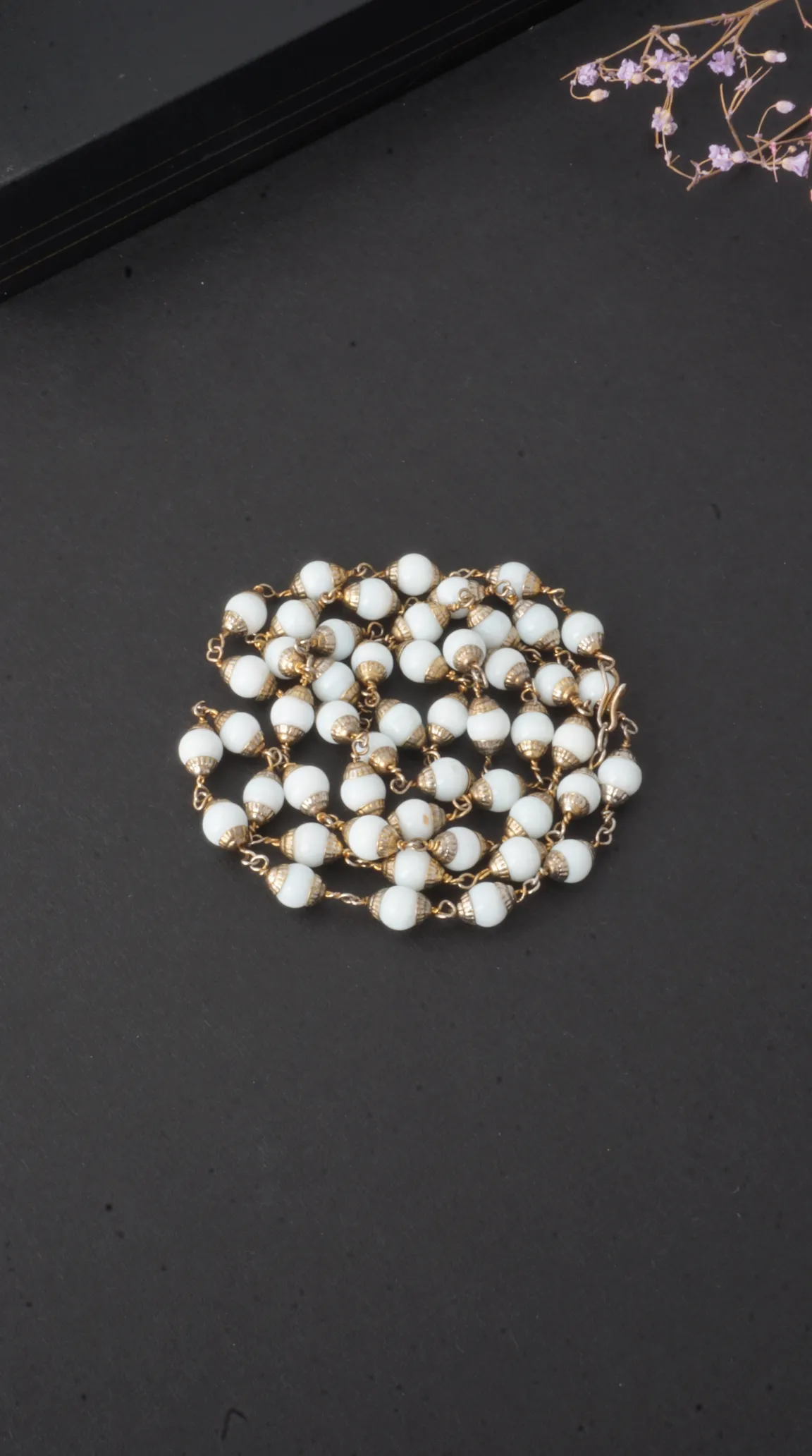 Vintage white beaded necklace with gold-tone caps on a dark background.