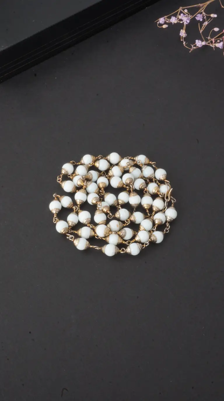 Vintage white beaded necklace with gold-tone caps on a dark background.