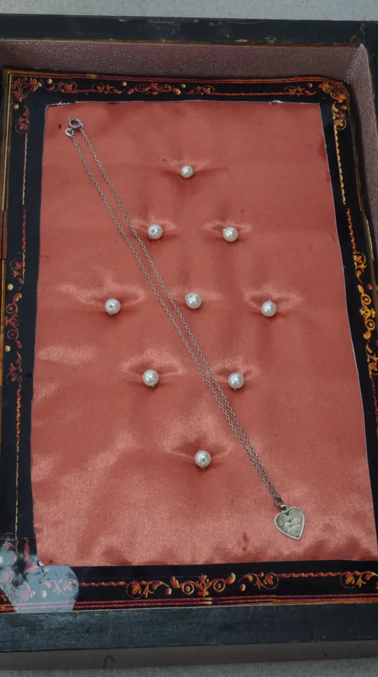 Vintage sterling silver heart pendant necklace on delicate chain displayed on tufted peach satin with pearl accents in an ornate antique jewelry box.