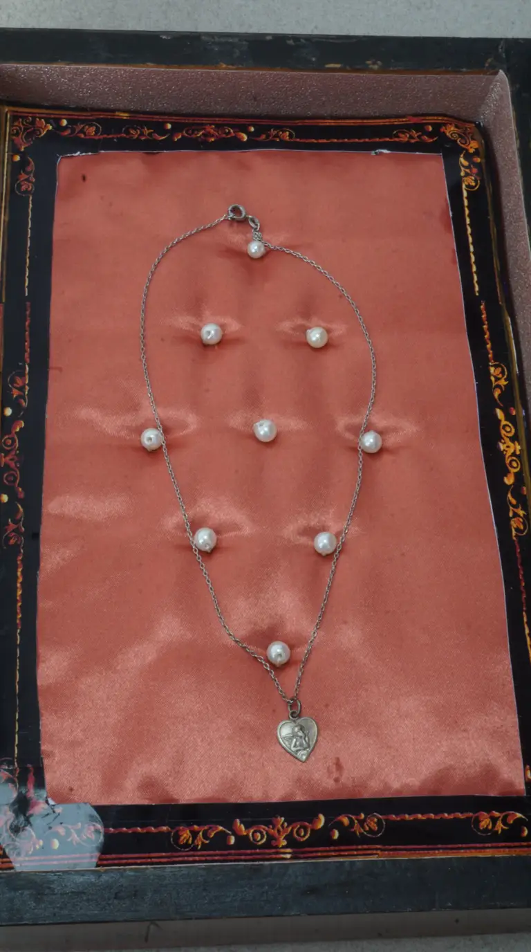 Vintage silver chain necklace with spaced pearls and heart cherub pendant on a salmon satin background in ornate box.