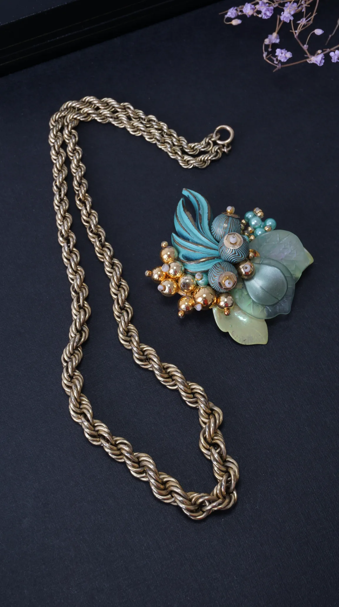 Vintage gold tone rope chain necklace and intricate teal, green, and gold floral brooch.