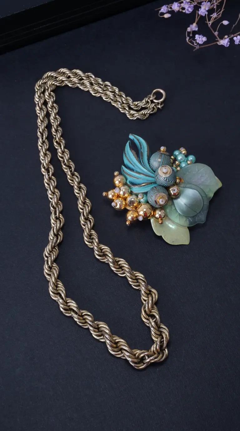 Vintage gold tone rope chain necklace and intricate teal, green, and gold floral brooch.