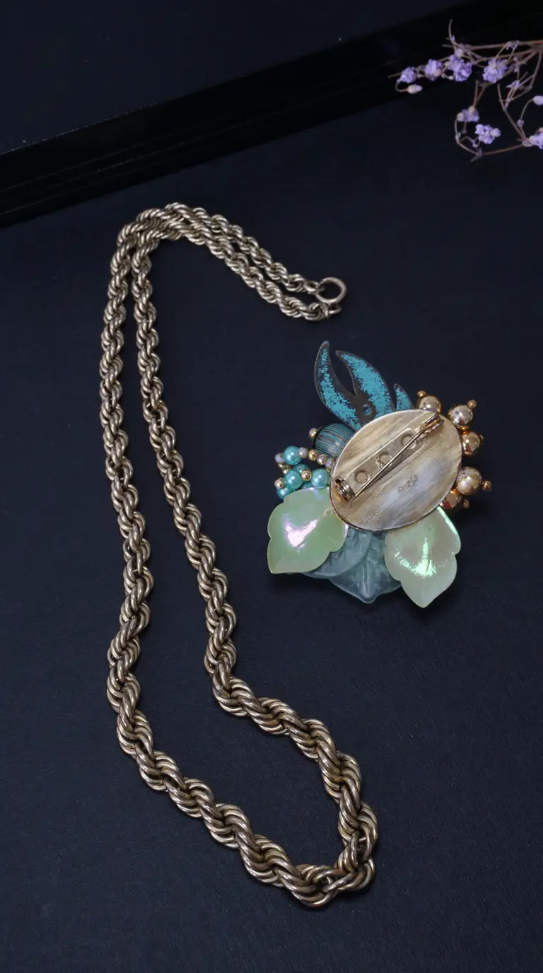 Vintage gold tone rope chain necklace and floral brooch with iridescent green leaves, turquoise accents, and pearl beads.