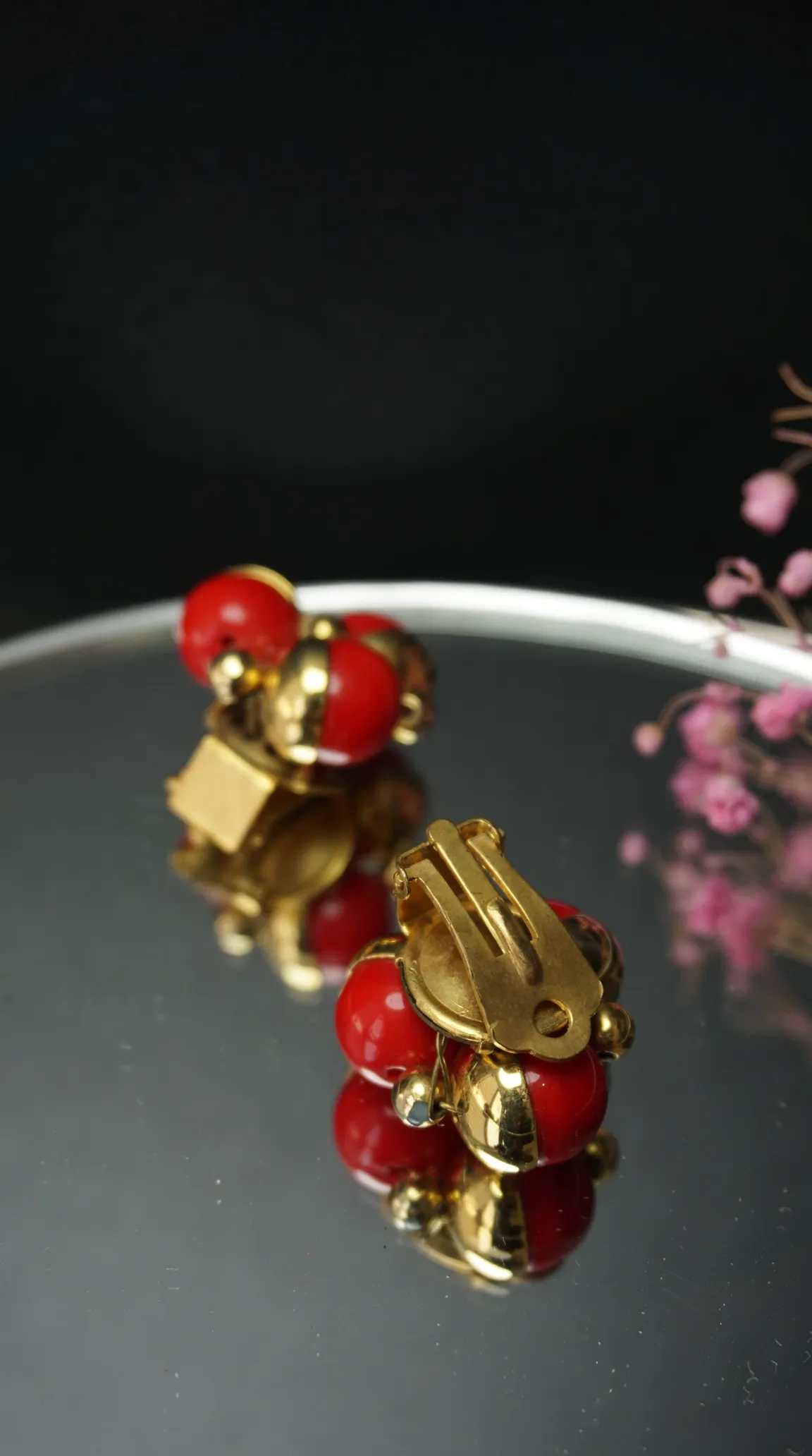Vintage gold tone clip-on earrings with red spherical beads and gold detailing on a reflective surface.