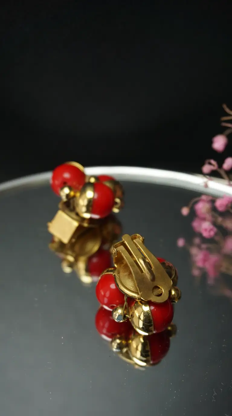 Vintage gold tone clip-on earrings with red spherical beads and gold detailing on a reflective surface.