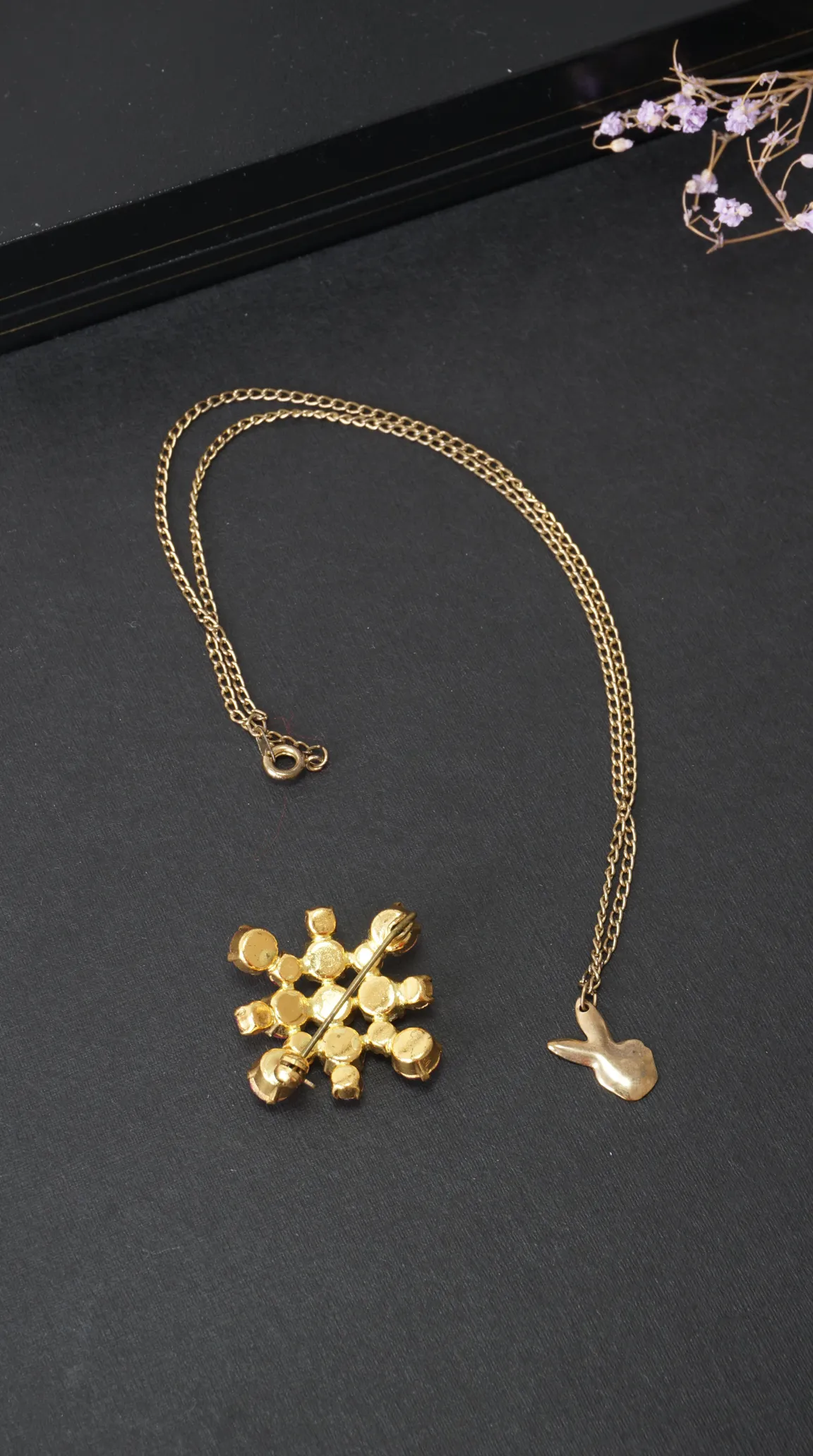 Vintage gold tone bunny pendant necklace and gold tone cluster brooch with pin, on black background.