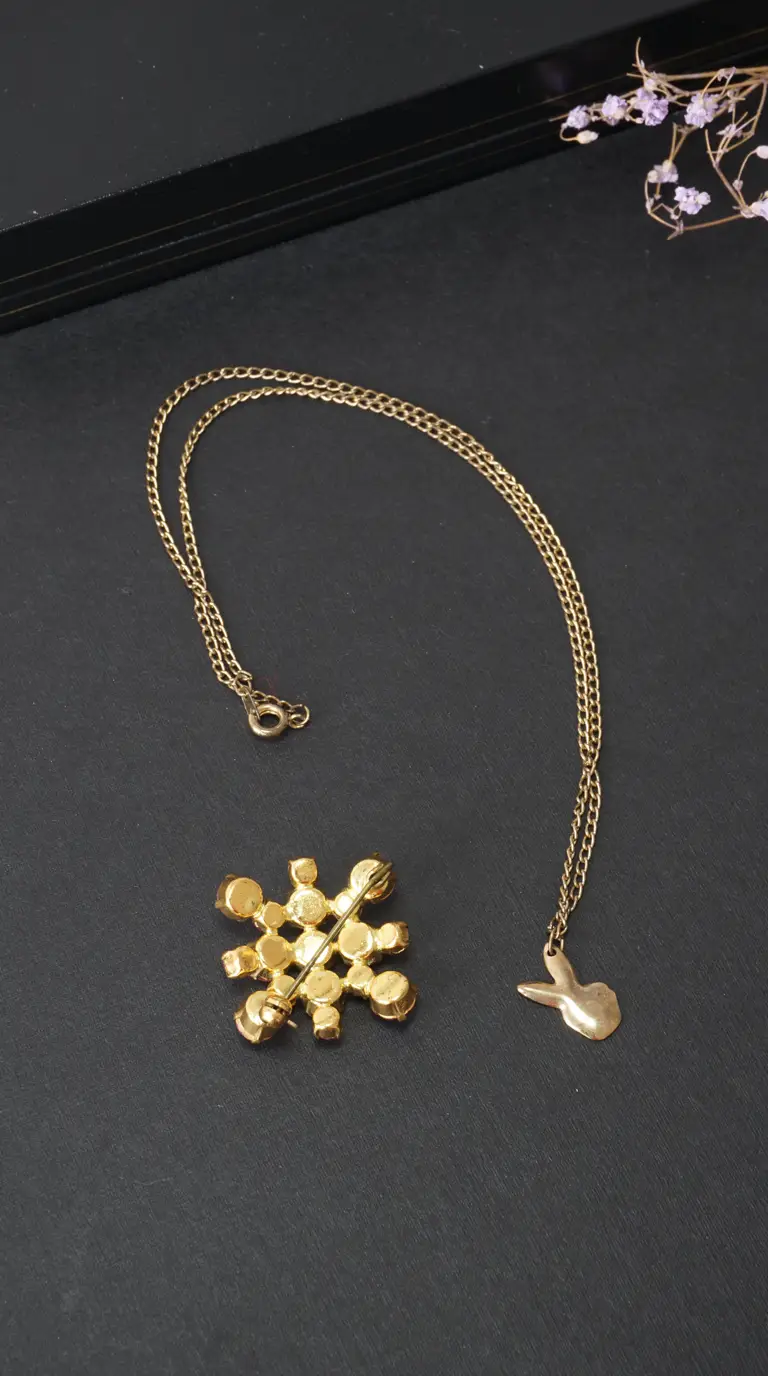 Vintage gold tone bunny pendant necklace and gold tone cluster brooch with pin, on black background.