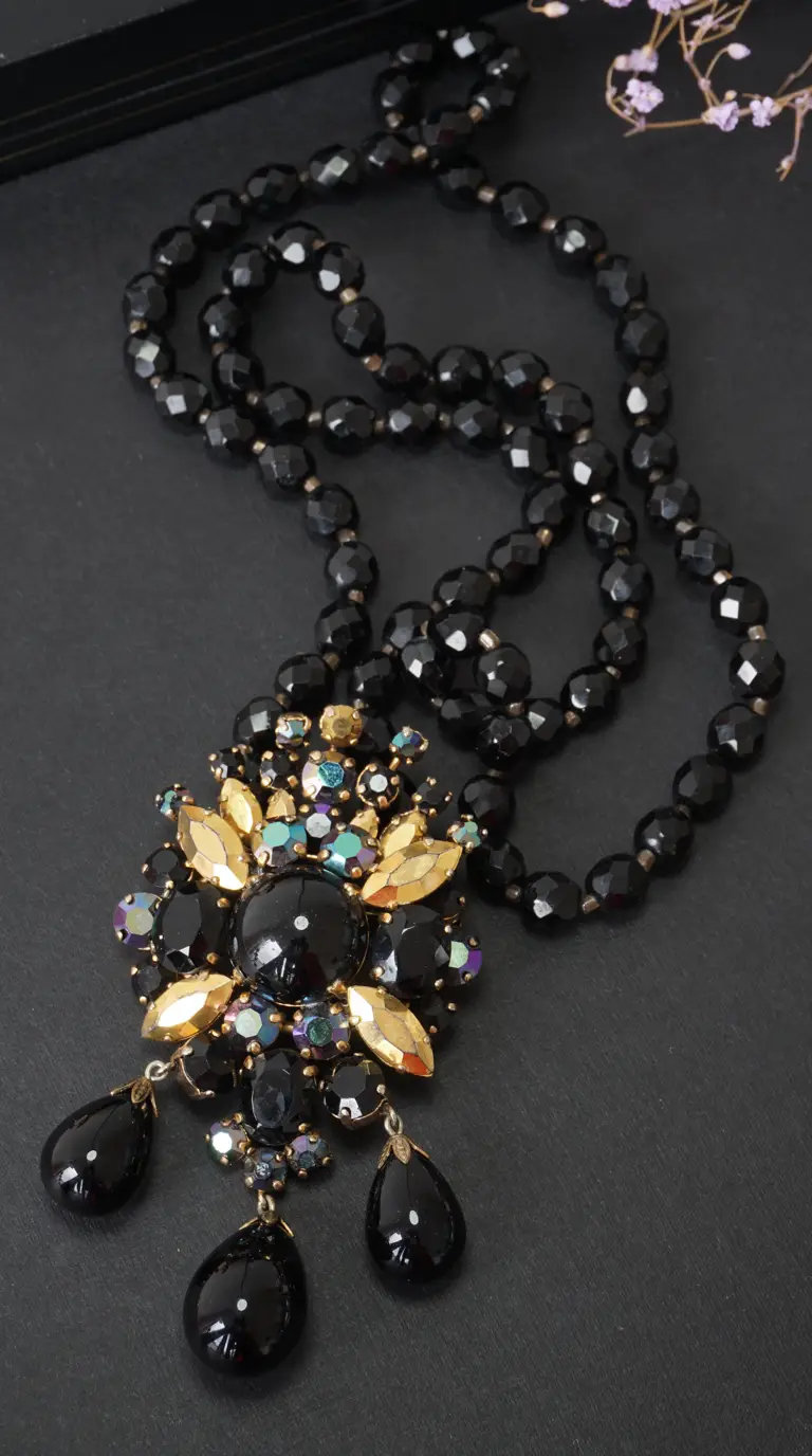 Vintage black faceted bead necklace with ornate gold, black, and iridescent rhinestone pendant featuring three black teardrop dangles.
