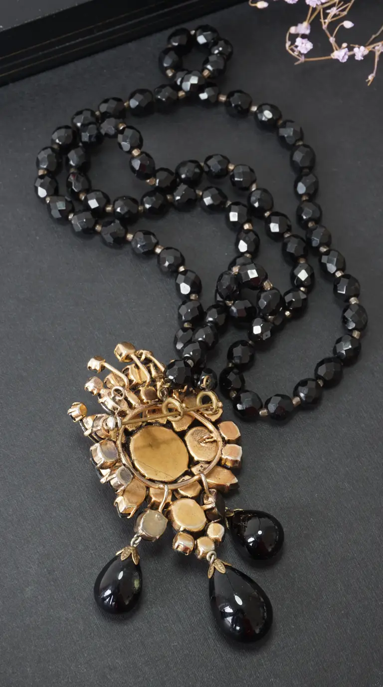 Vintage long black faceted bead necklace with ornate gold-tone pendant with black teardrop dangles