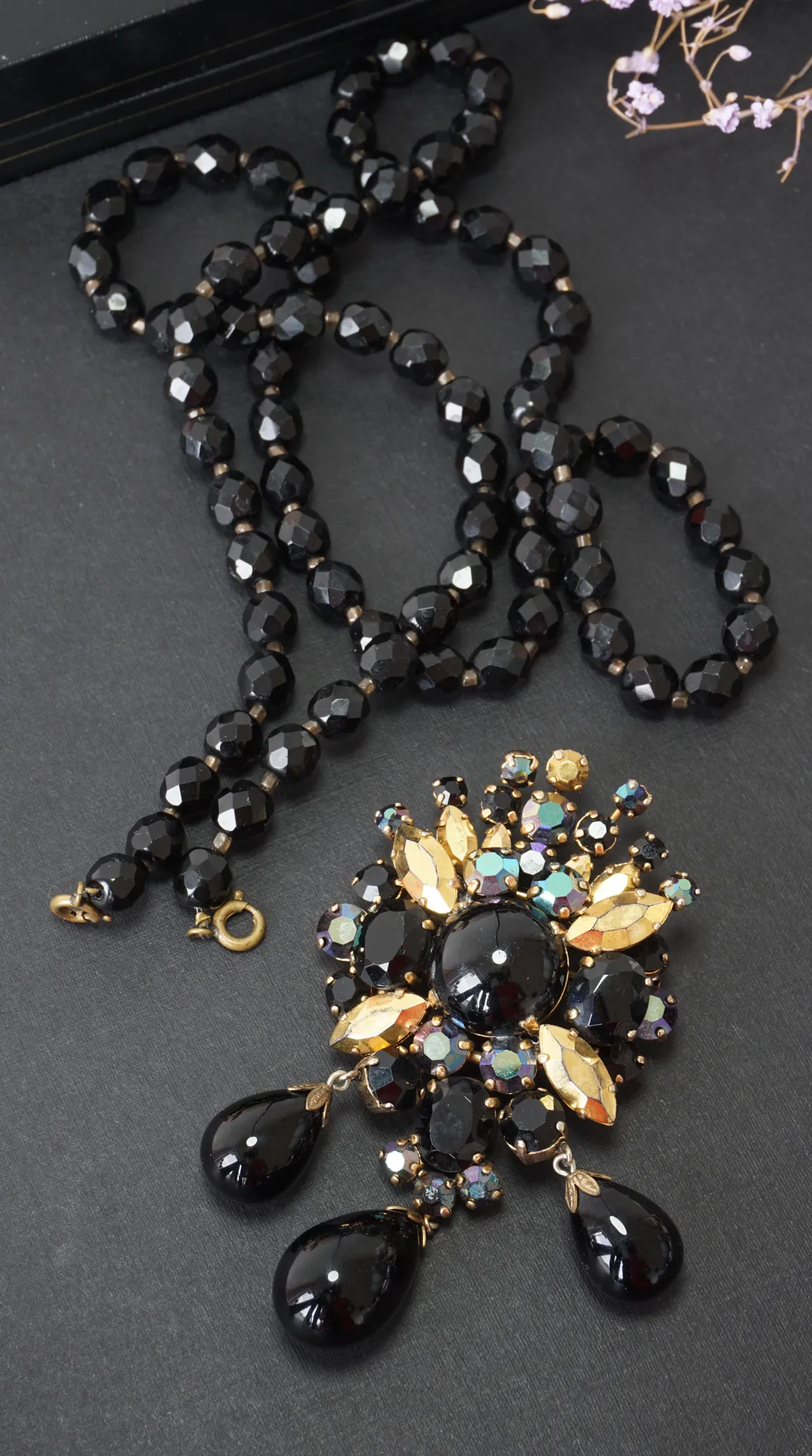 Vintage black faceted glass bead necklace and large ornate black, gold, and iridescent rhinestone brooch with dangling black teardrop gems.