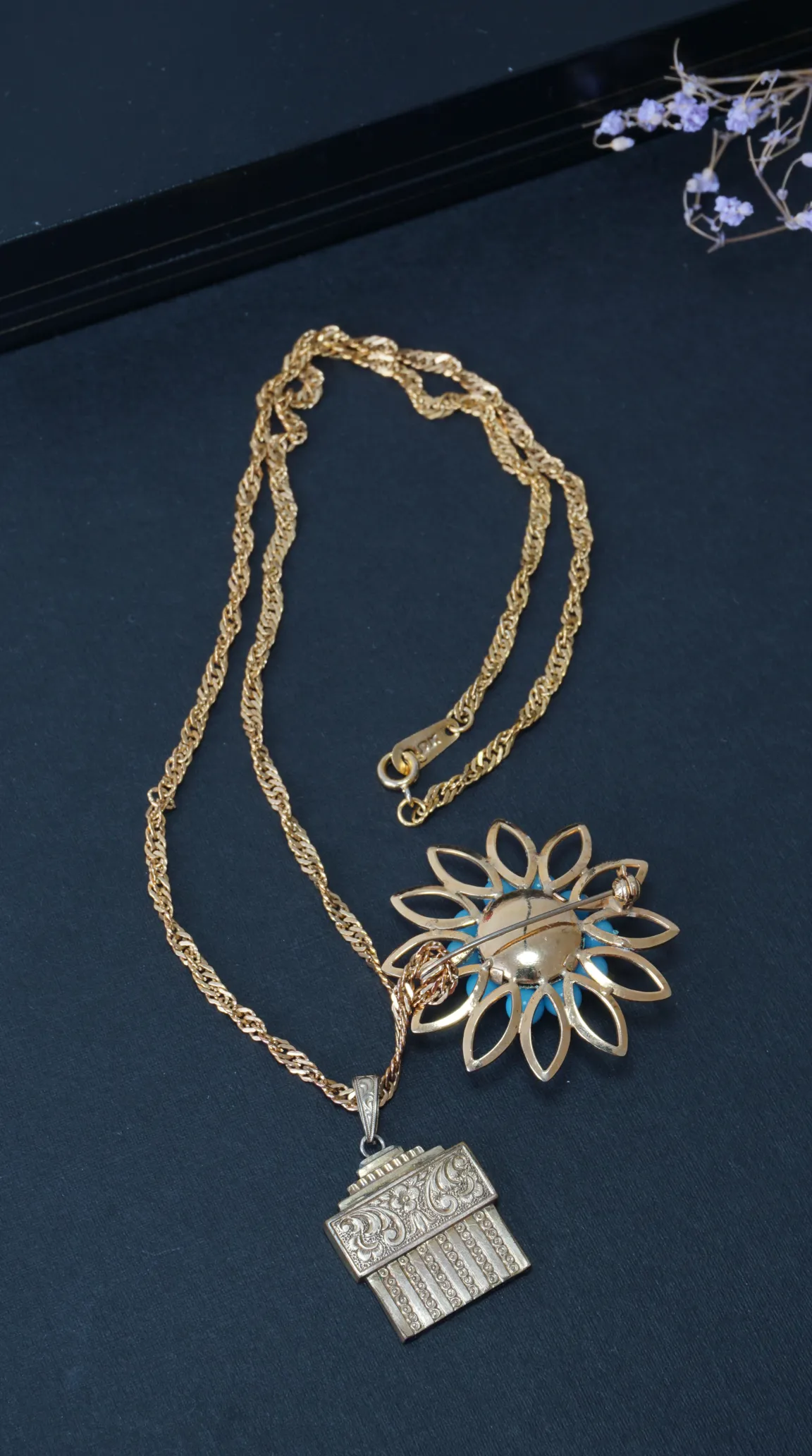 Vintage 10K gold necklace with ornate Art Deco rectangular pendant and floral brooch with blue accents on a dark surface.