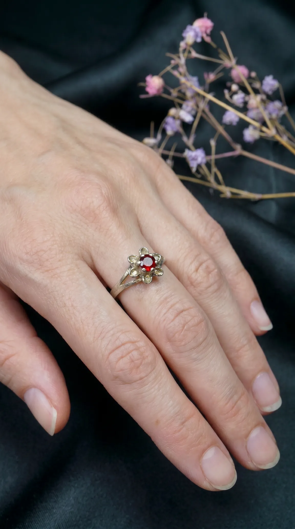Vintage silver floral ring with red gemstone worn on a hand
