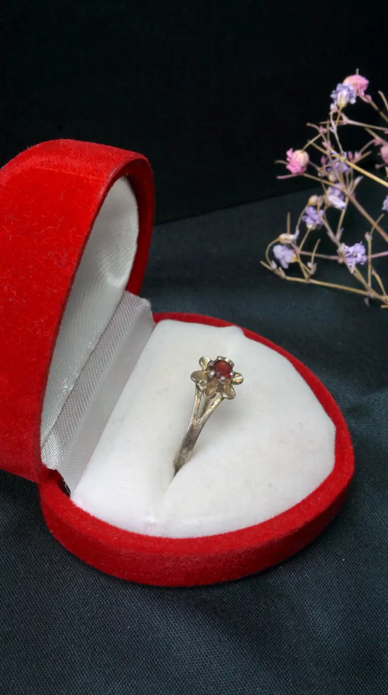 Vintage silver ring with red garnet gemstone in floral setting, inside an open red velvet jewelry box.