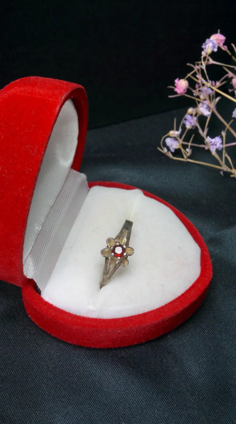 Vintage red gemstone flower ring in antique silver finish, displayed in an open red velvet heart jewelry box.