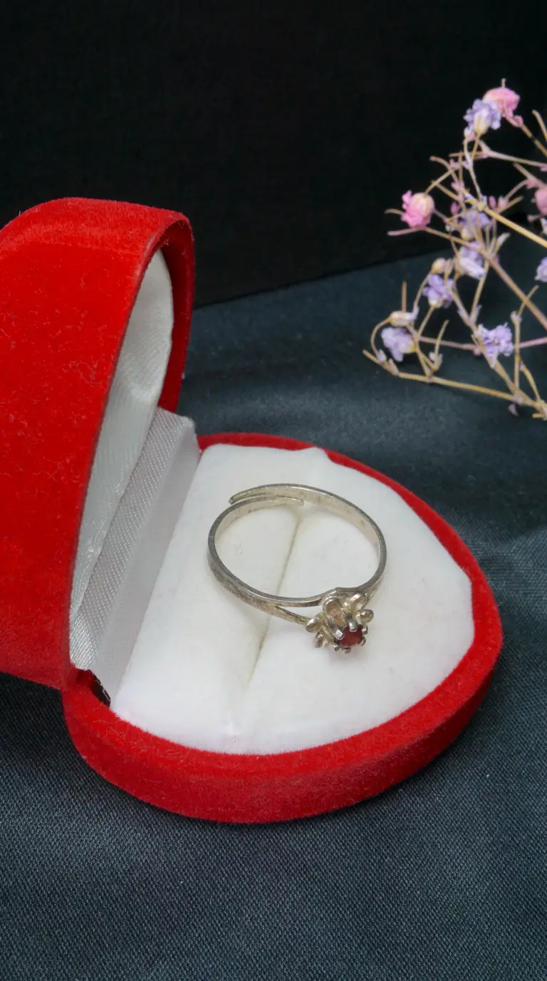 Vintage adjustable silver ring with red garnet gemstone and floral setting, in an open red heart-shaped velvet box.