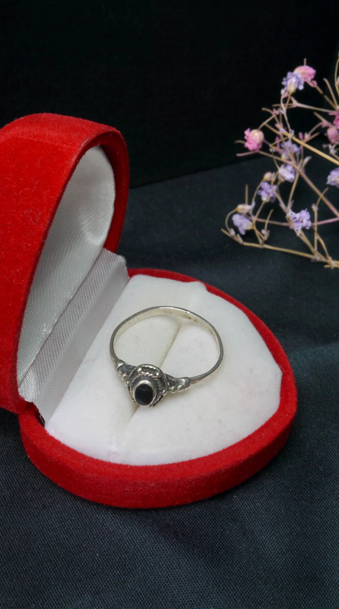 Vintage sterling silver ring with black onyx gemstone and intricate filigree detail in a red velvet jewelry box.