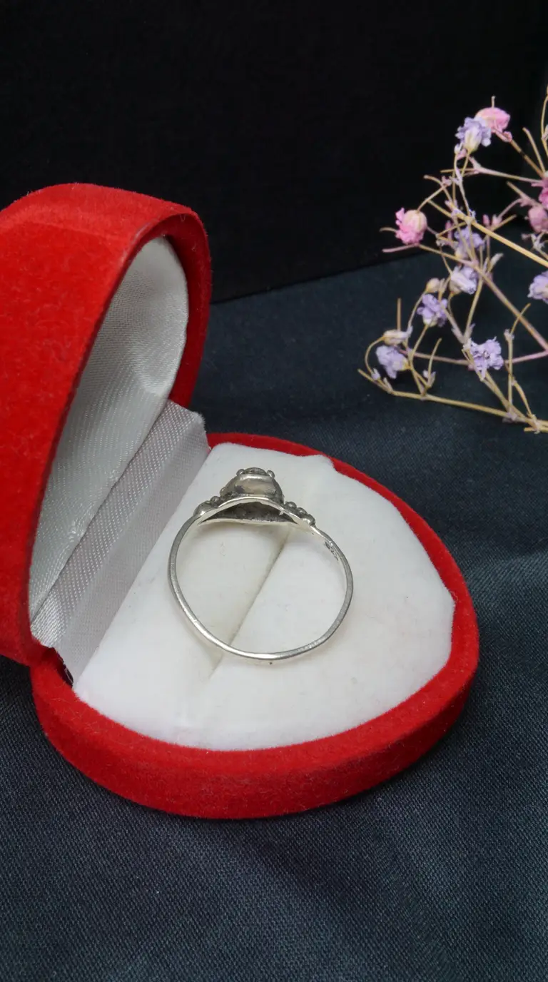 Vintage sterling silver ring with ornate gemstone setting in open red velvet gift box, dark background with dried lavender flowers.