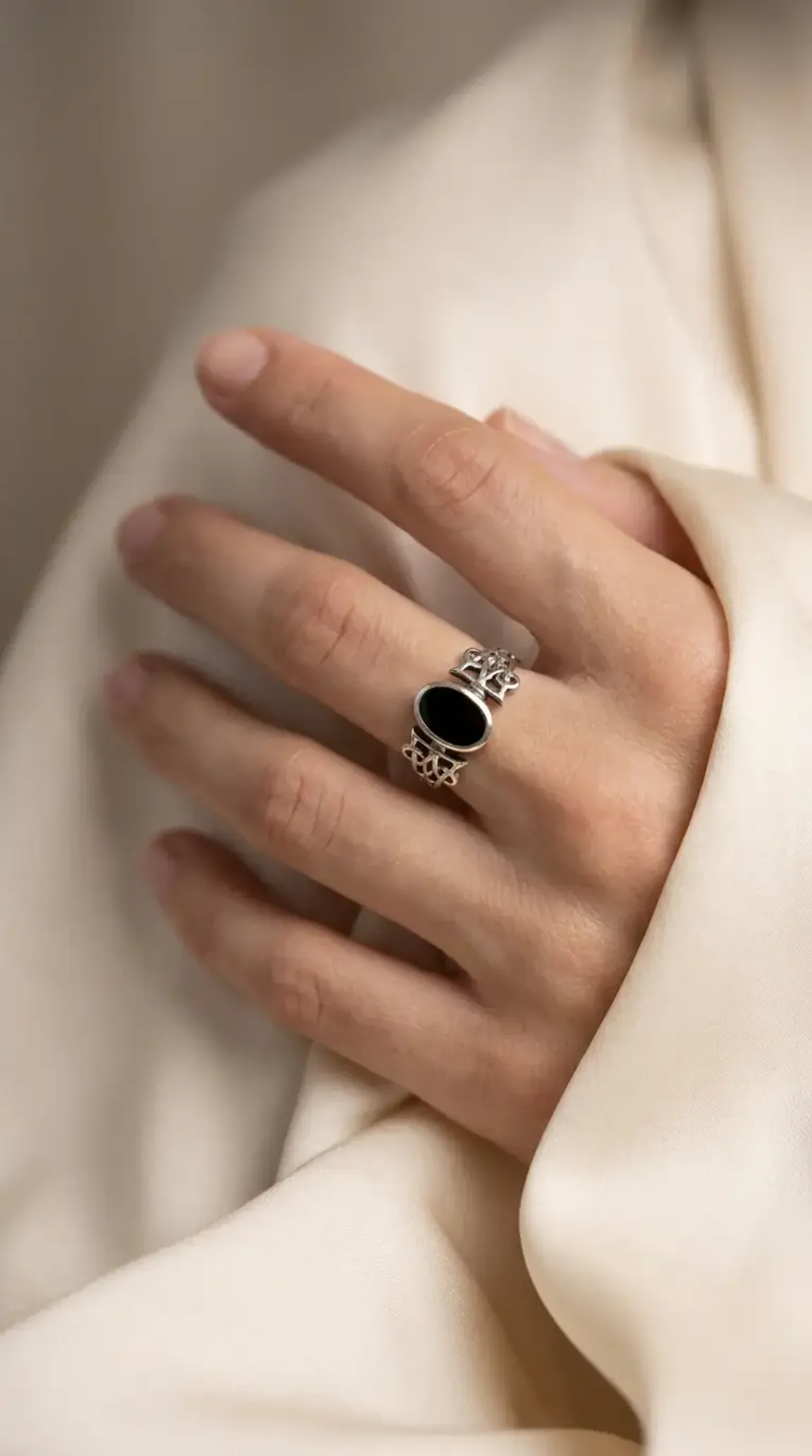 Vintage sterling silver ring with oval black onyx gemstone and ornate band design on a hand.