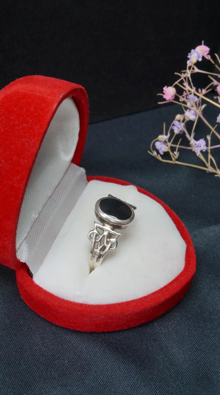 Vintage sterling silver ring with oval black onyx gemstone and ornate band in a red velvet jewelry box.