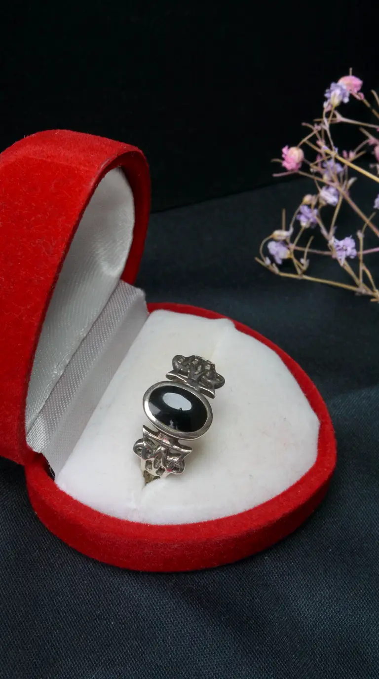 Vintage silver ring with black onyx gemstone and ornate details in red velvet jewelry box