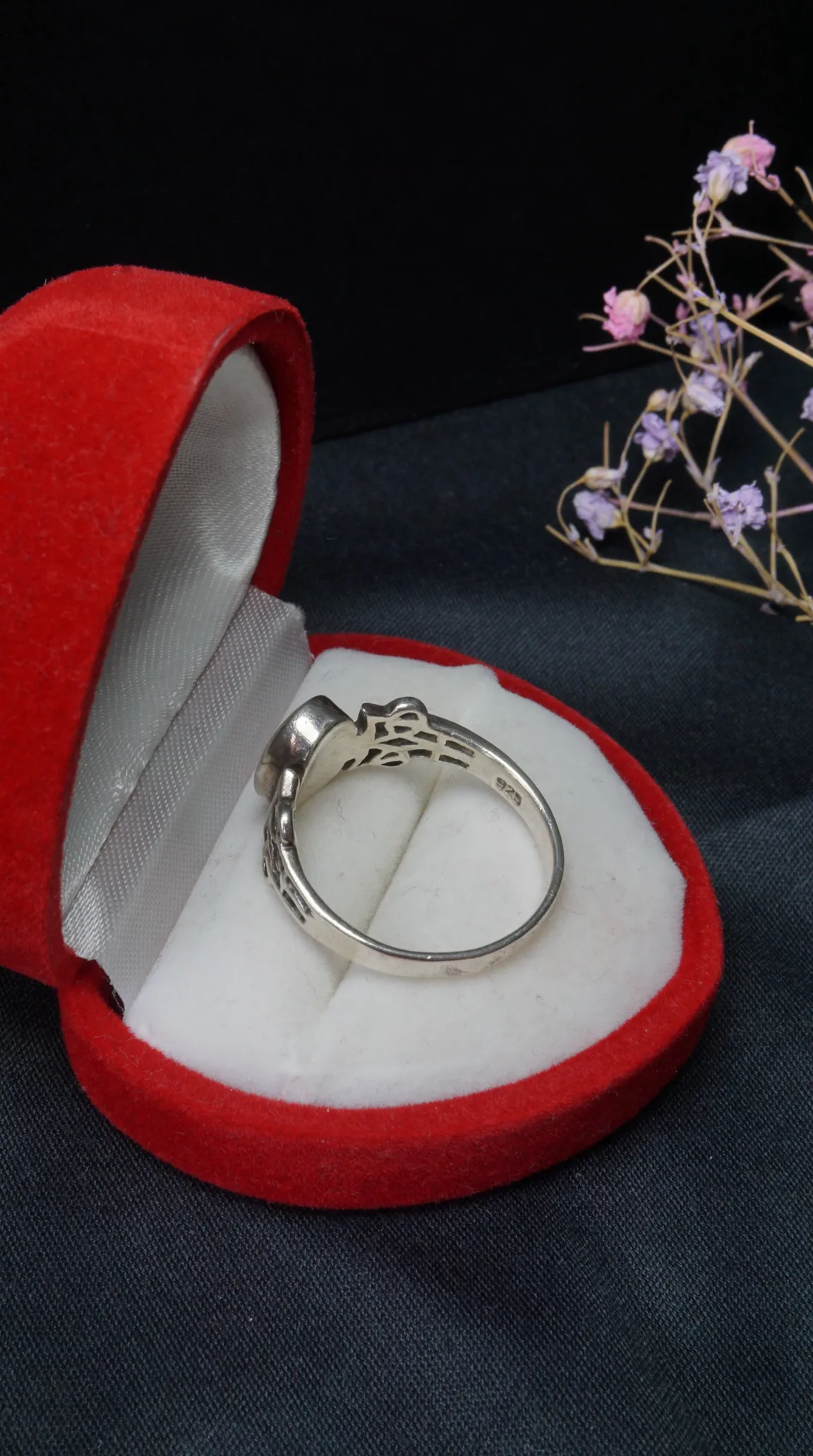 Vintage sterling silver 925 ring with intricate filigree band design in an open red velvet heart-shaped jewelry box, on a dark background with dried flowers.