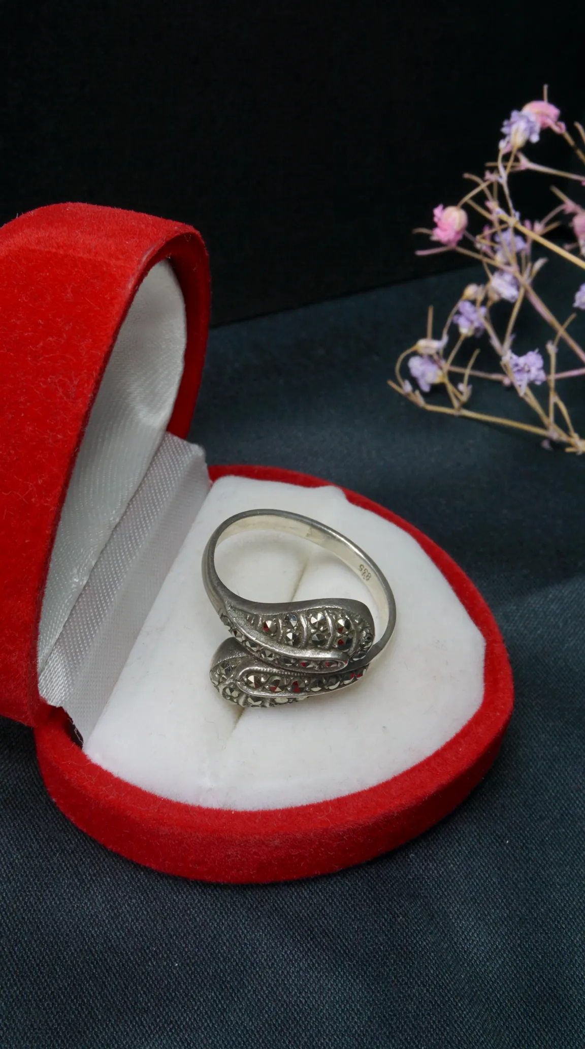 Vintage 835 silver ring with marcasite and red gemstones, featuring an ornate wrap-around design, displayed in a red heart-shaped jewelry box.