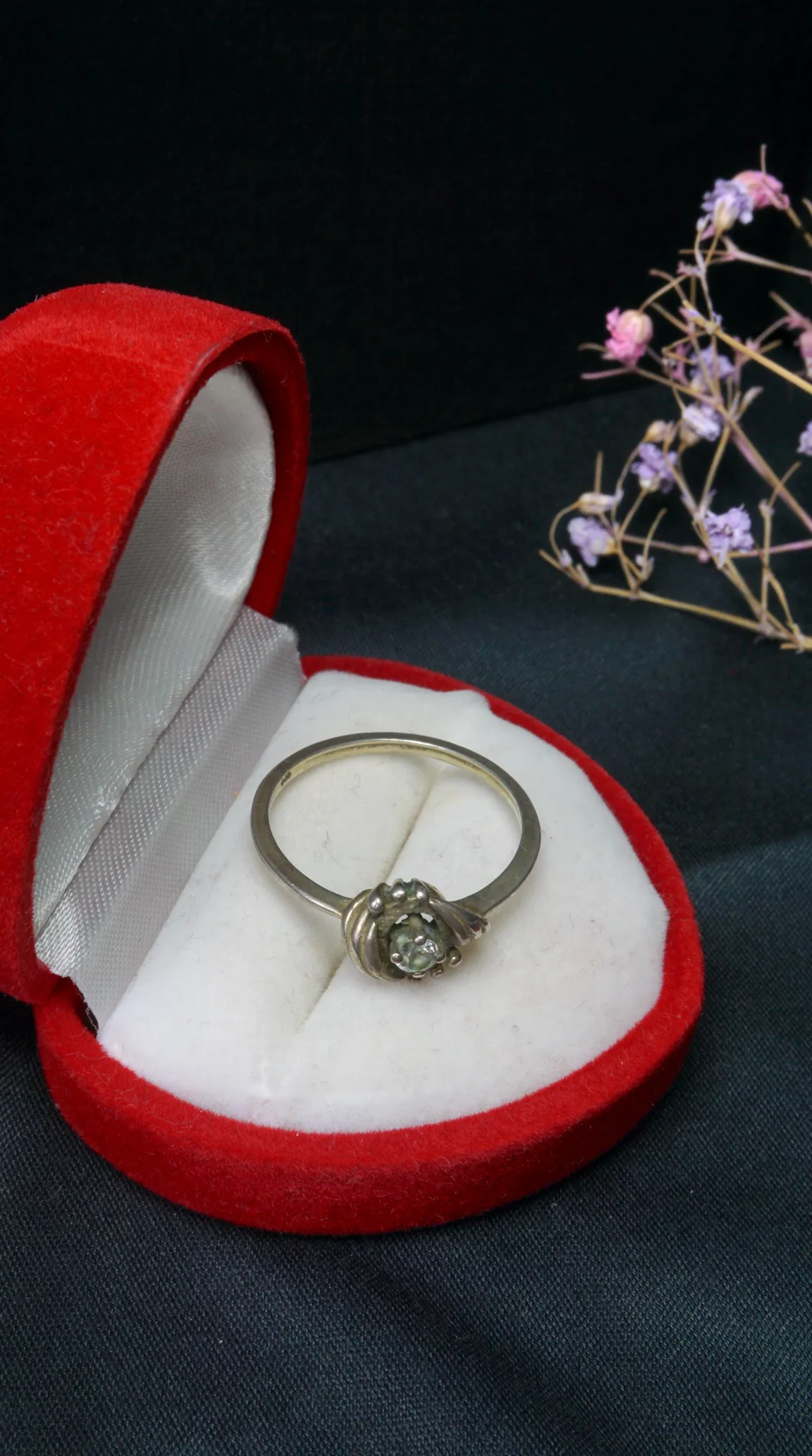 Antique silver ring with sparkling light gemstone in unique setting, presented in red velvet jewelry box.