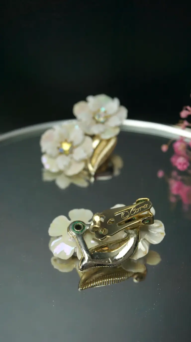 Vintage Cora mother-of-pearl floral clip-on earrings with iridescent petals, sparkling rhinestones, and gold-tone setting.