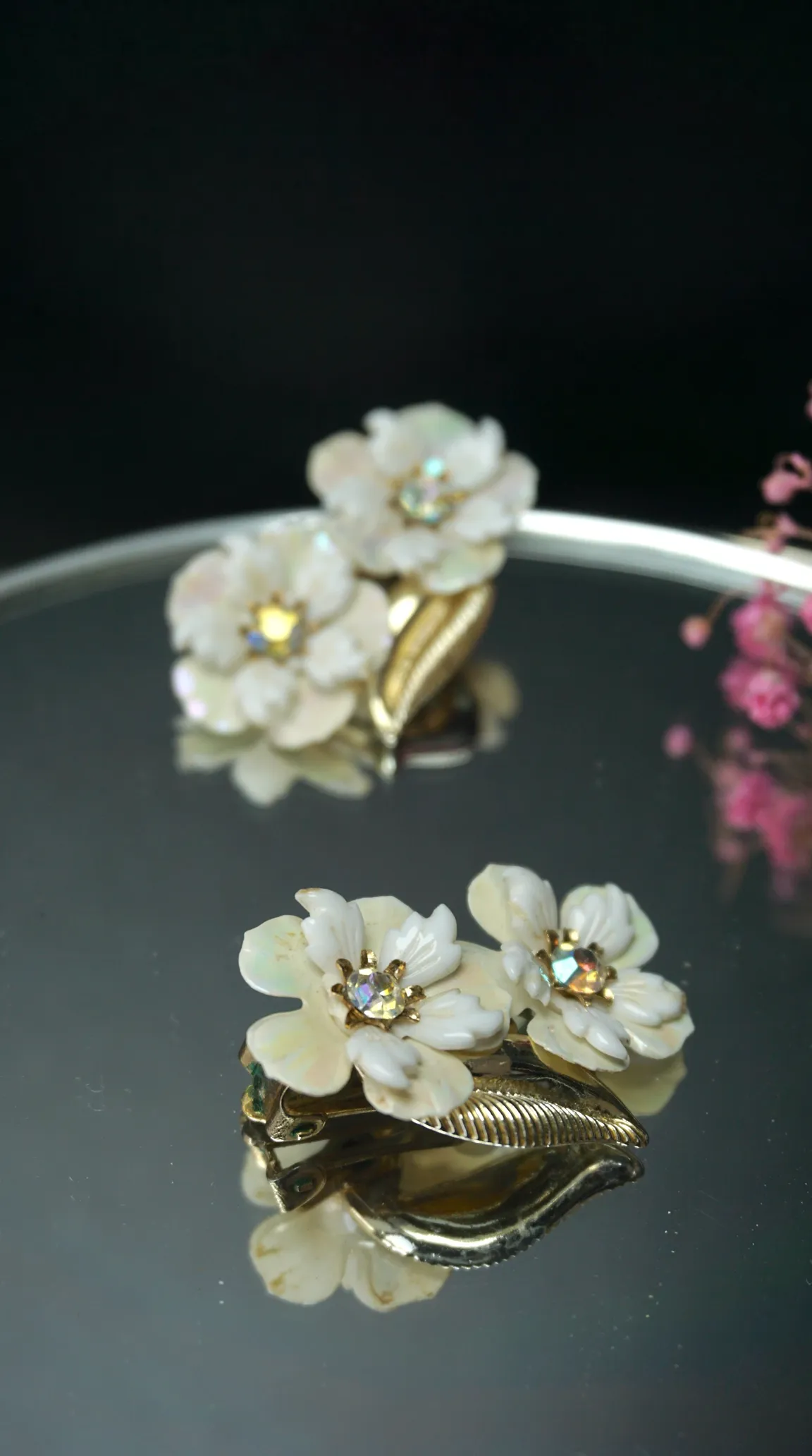 Vintage white flower clip-on earrings with iridescent crystal centers and gold-tone leaf accents.