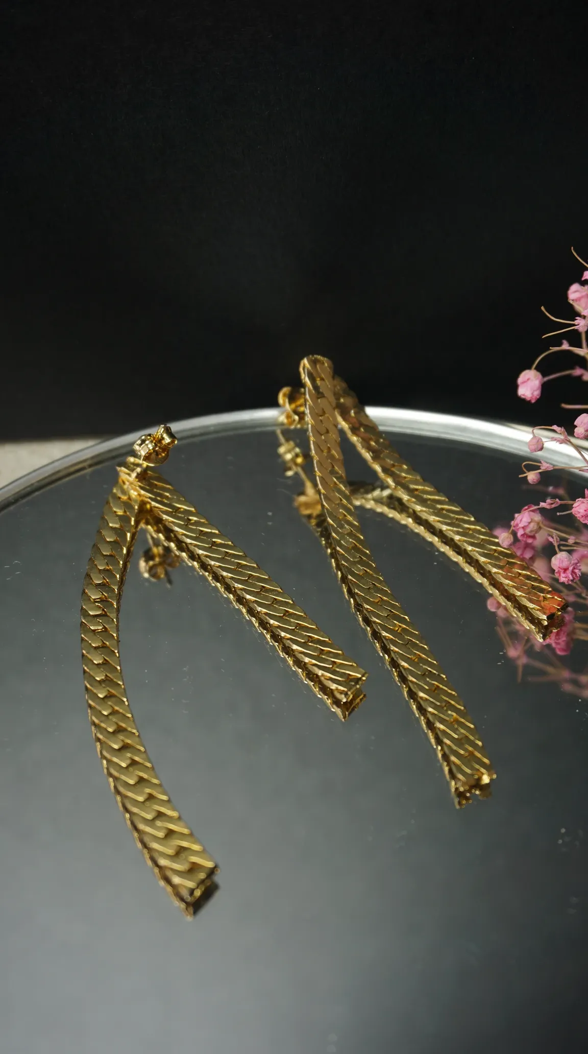 Vintage gold herringbone chain dangle earrings on mirrored surface