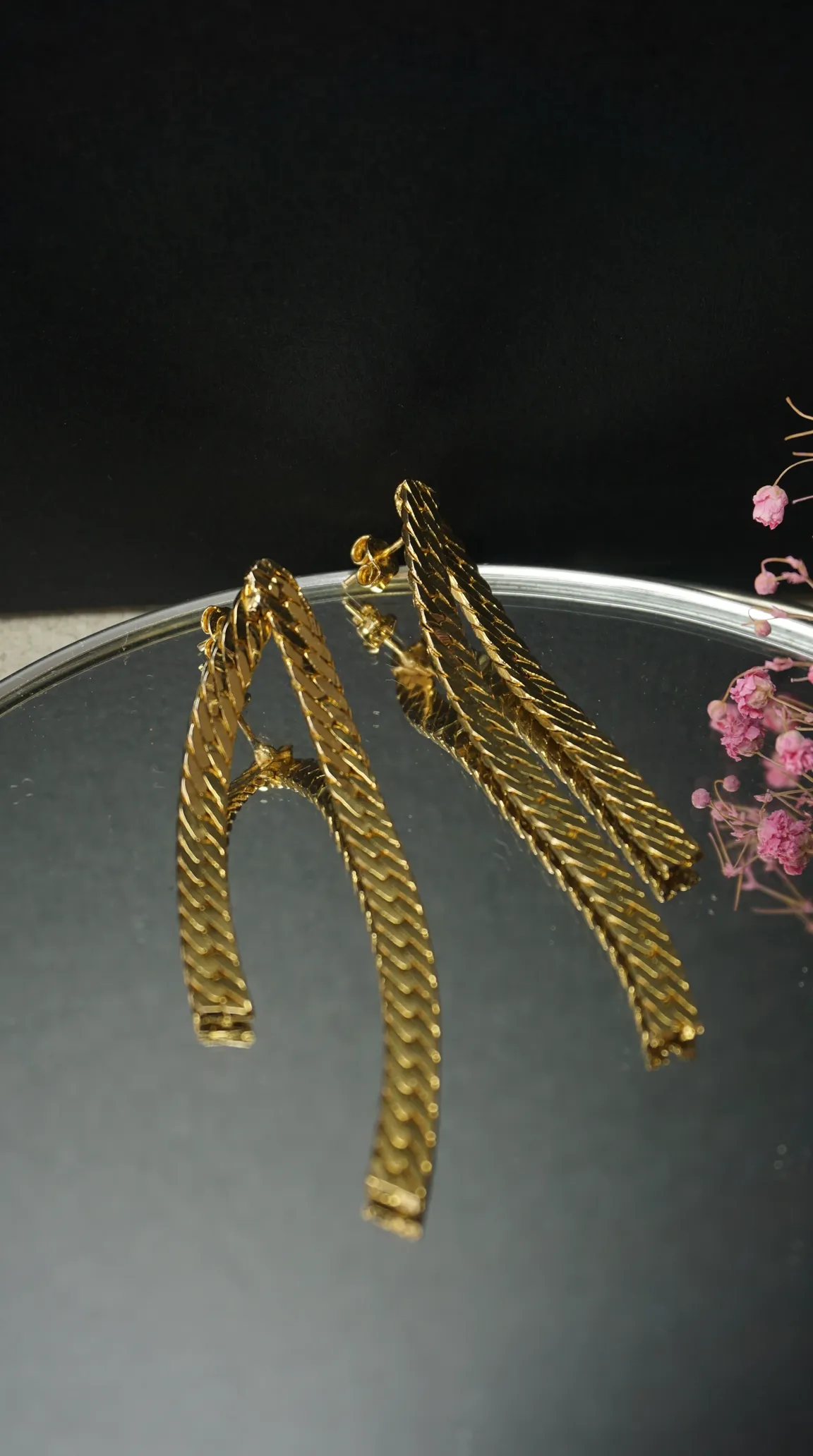 Vintage gold herringbone chain dangle earrings on a mirrored tray with pink dried flowers