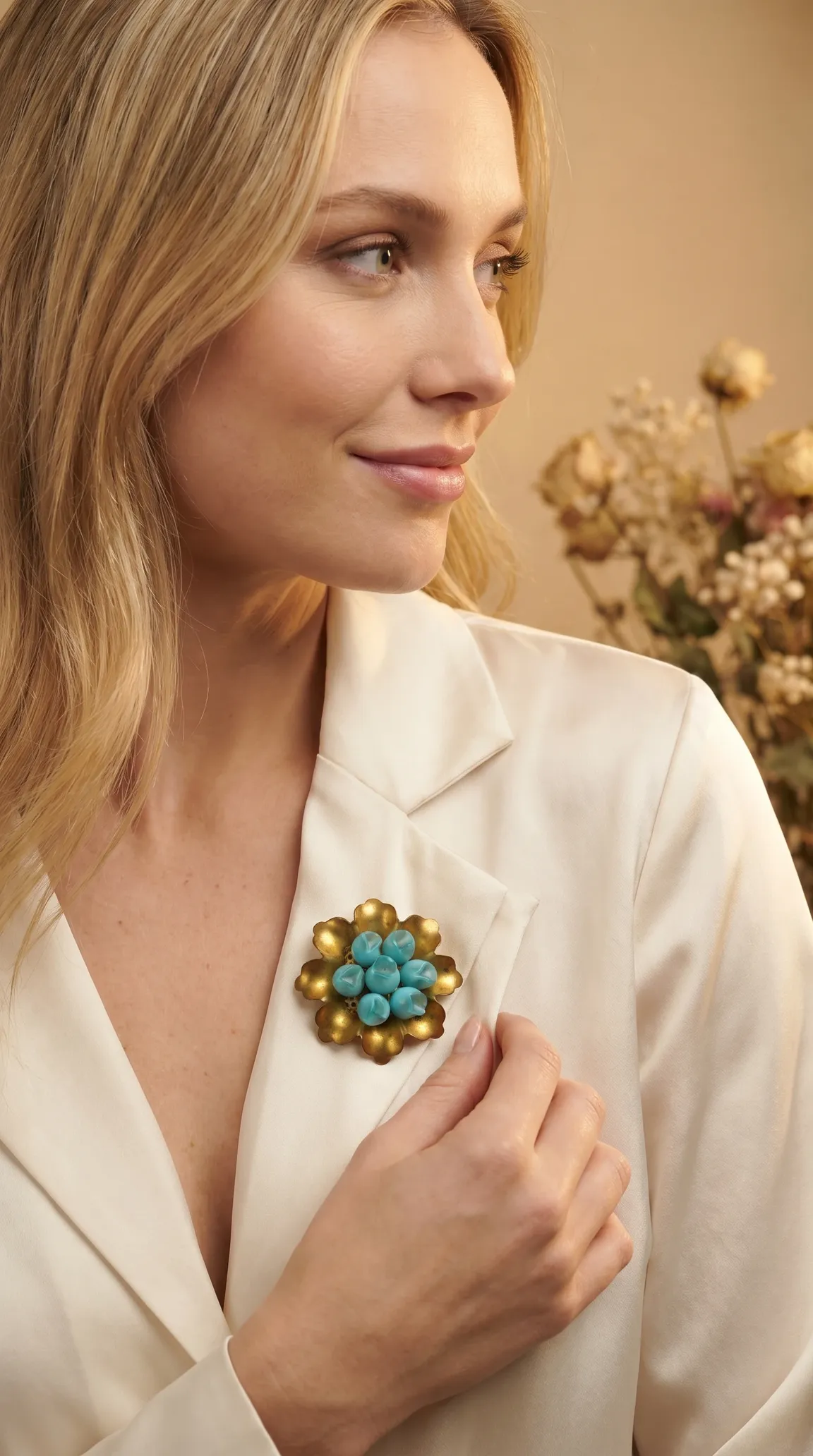 Vintage gold tone floral brooch with turquoise beads on a woman's cream satin jacket.