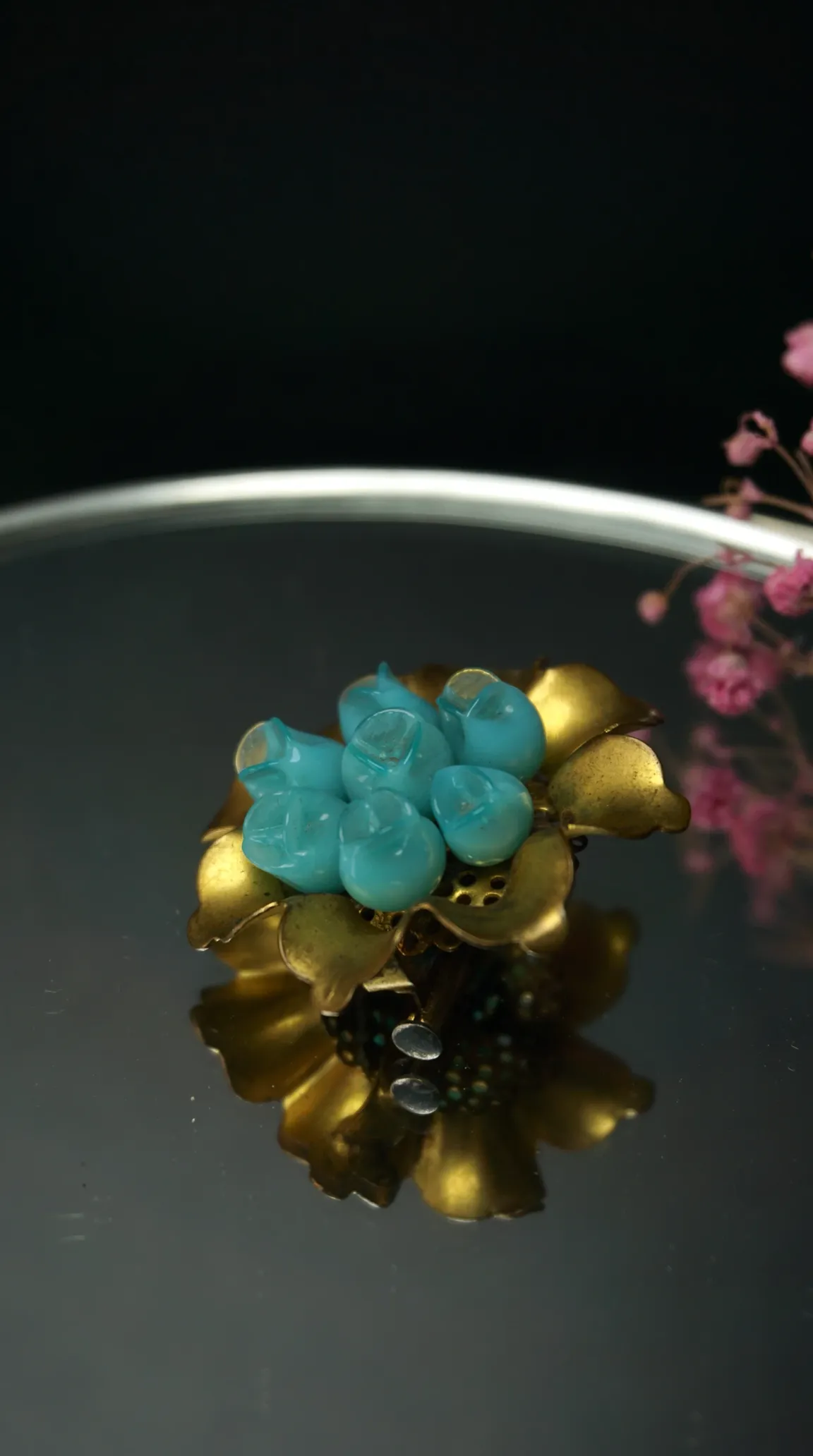 Vintage gold tone flower brooch with turquoise blue flower buds, reflecting on a dark polished surface.