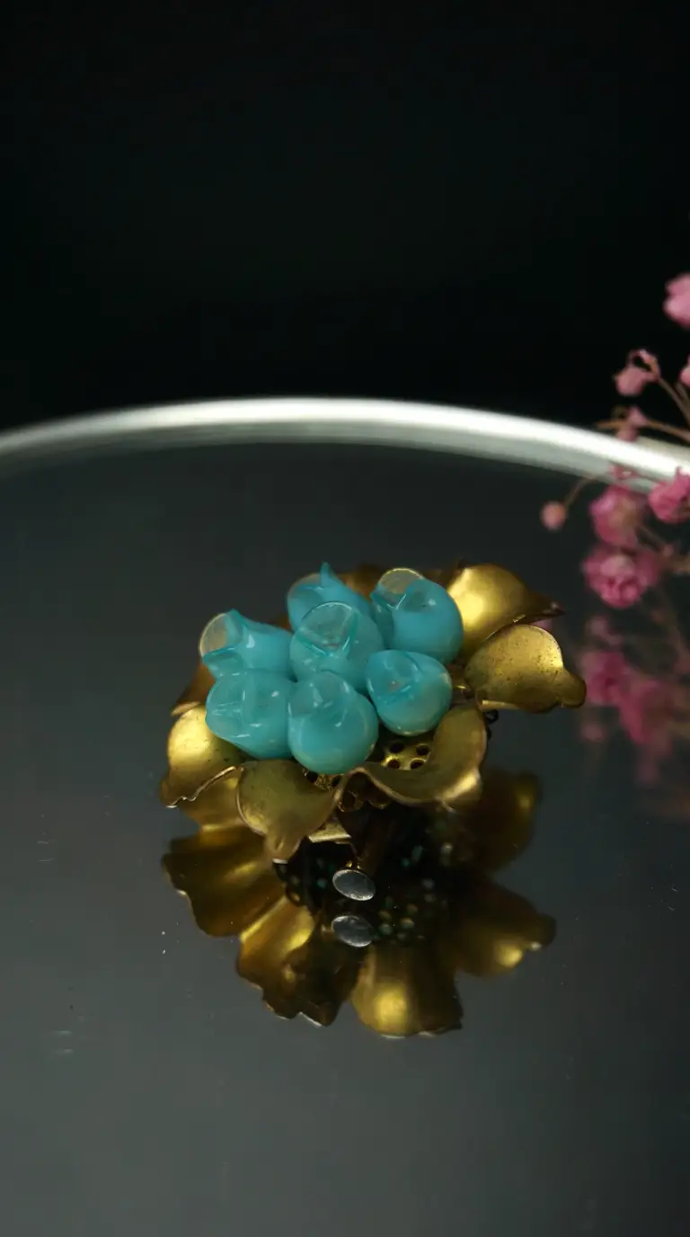 Vintage gold tone flower brooch with turquoise blue flower buds, reflecting on a dark polished surface.