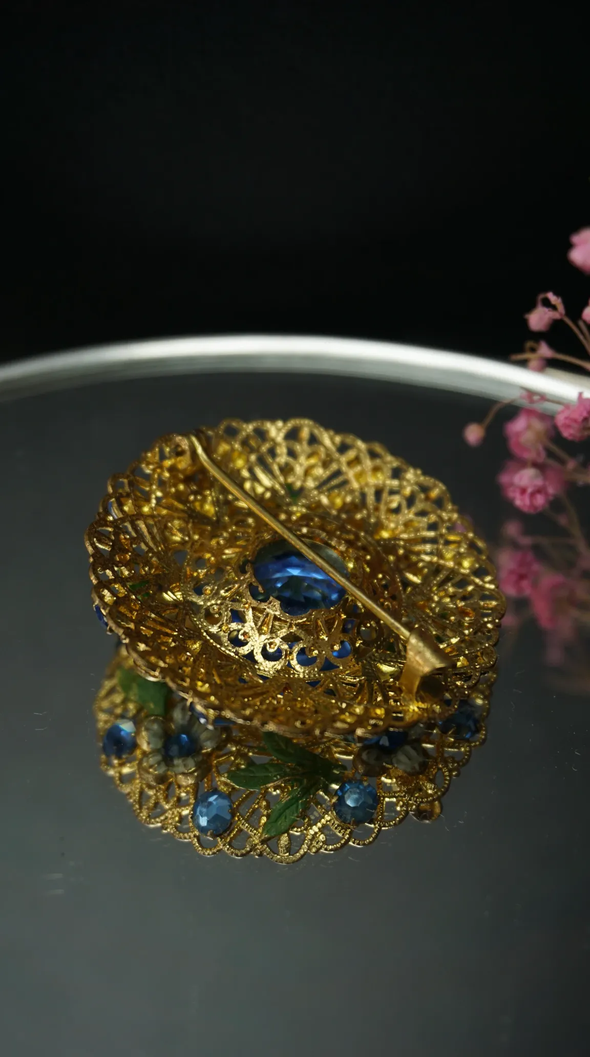 vintage gold filigree brooch with blue rhinestones, back view showing pin mechanism on reflective surface