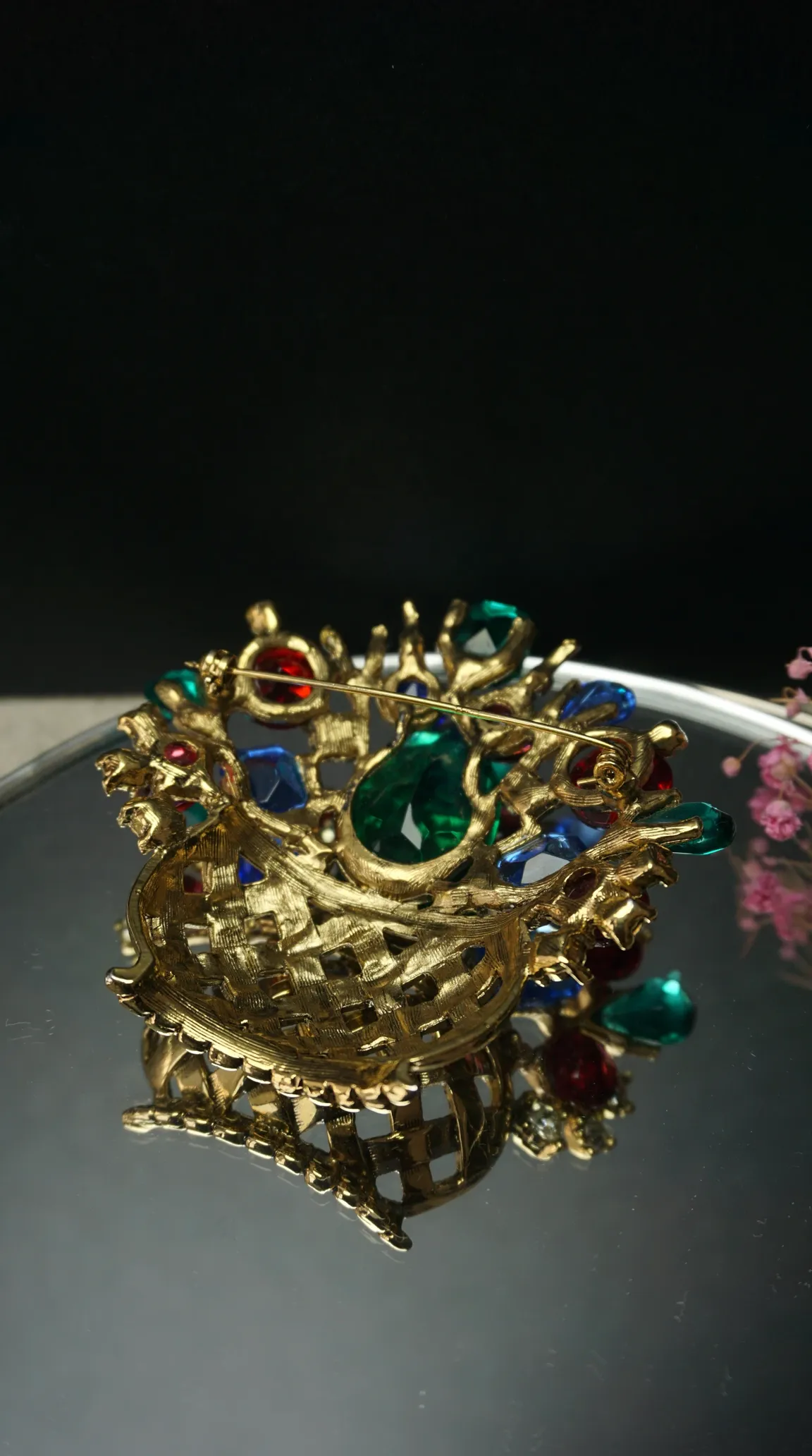 Vintage gold-toned basket brooch with red, green, and blue colorful gemstones on a reflective surface.