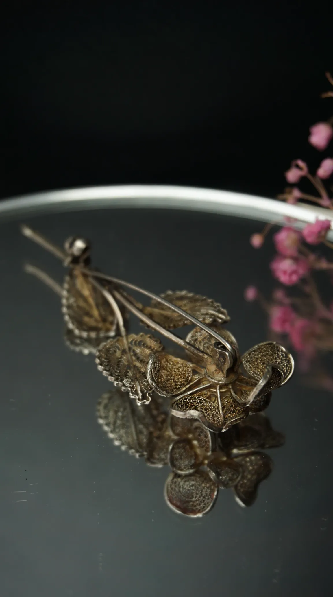 Vintage silver filigree flower brooch with delicate leaves, reflected on a dark surface, vintage floral pin.