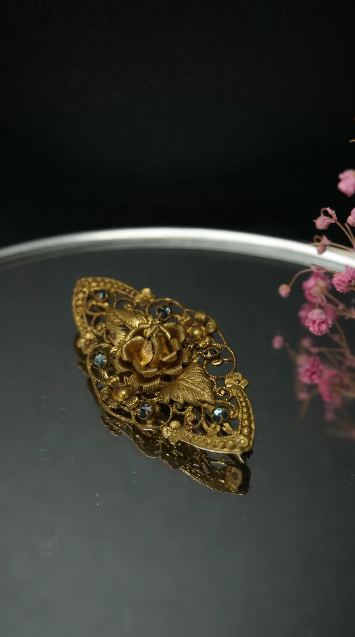 Vintage gold tone filigree brooch featuring a rose and leaf design, adorned with blue rhinestones, antique jewelry piece.