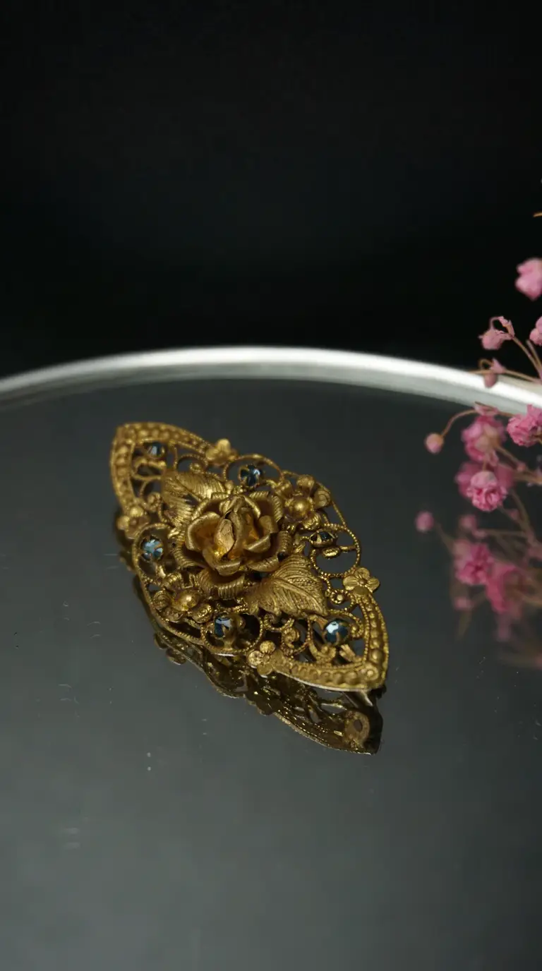Vintage gold tone filigree brooch featuring a rose and leaf design, adorned with blue rhinestones, antique jewelry piece.