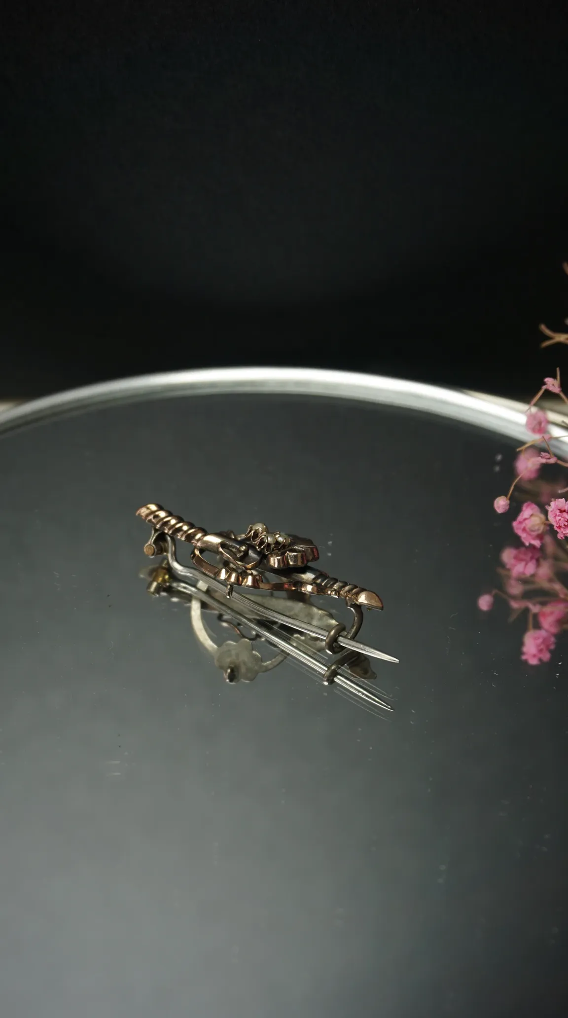 Vintage gold-tone crossed sword brooch with pearl details on a reflective surface.