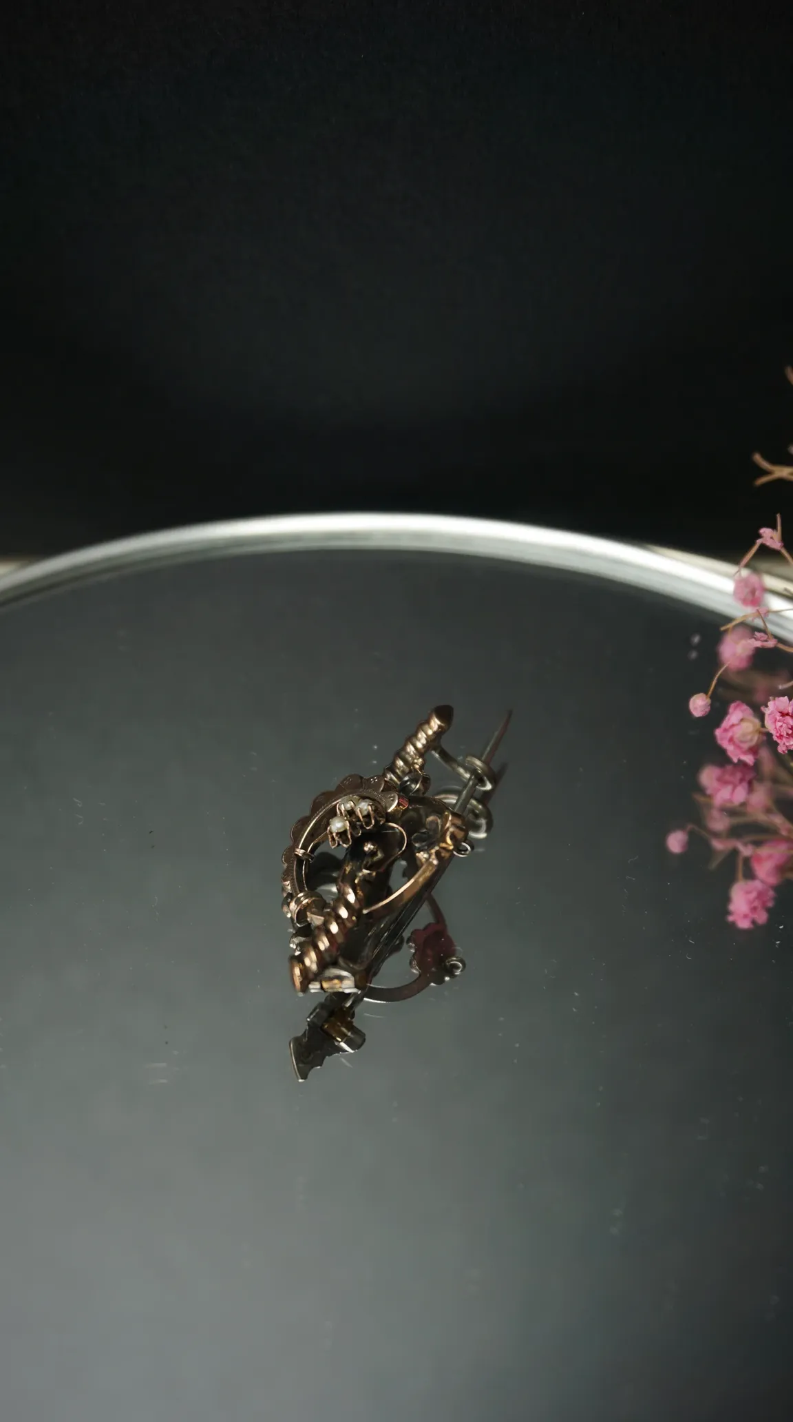 Vintage ornate antique gold tone brooch with seed pearls on a reflective surface with pink flowers