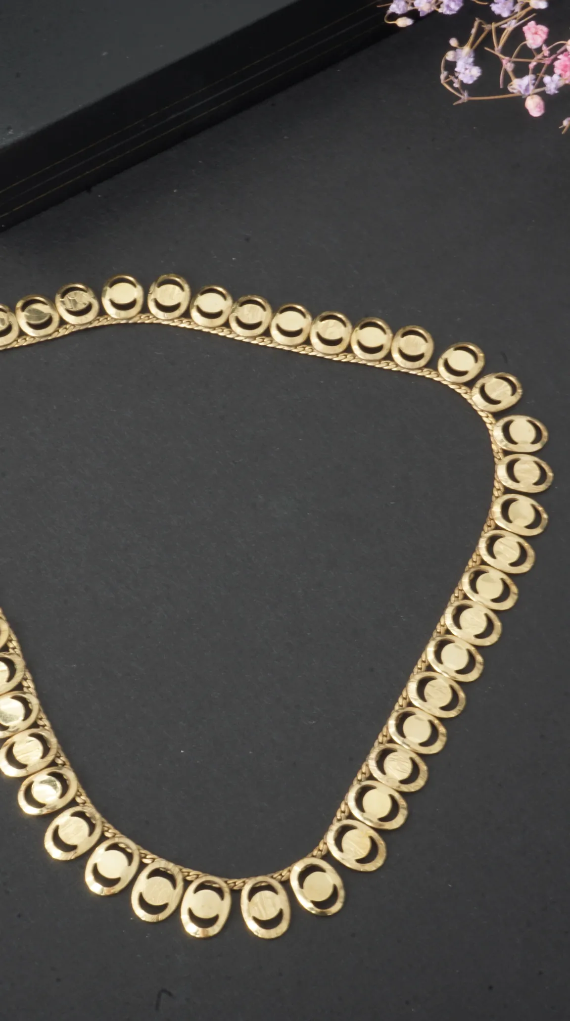 Vintage gold necklace with oval links and crescent moon cutouts on a dark background.