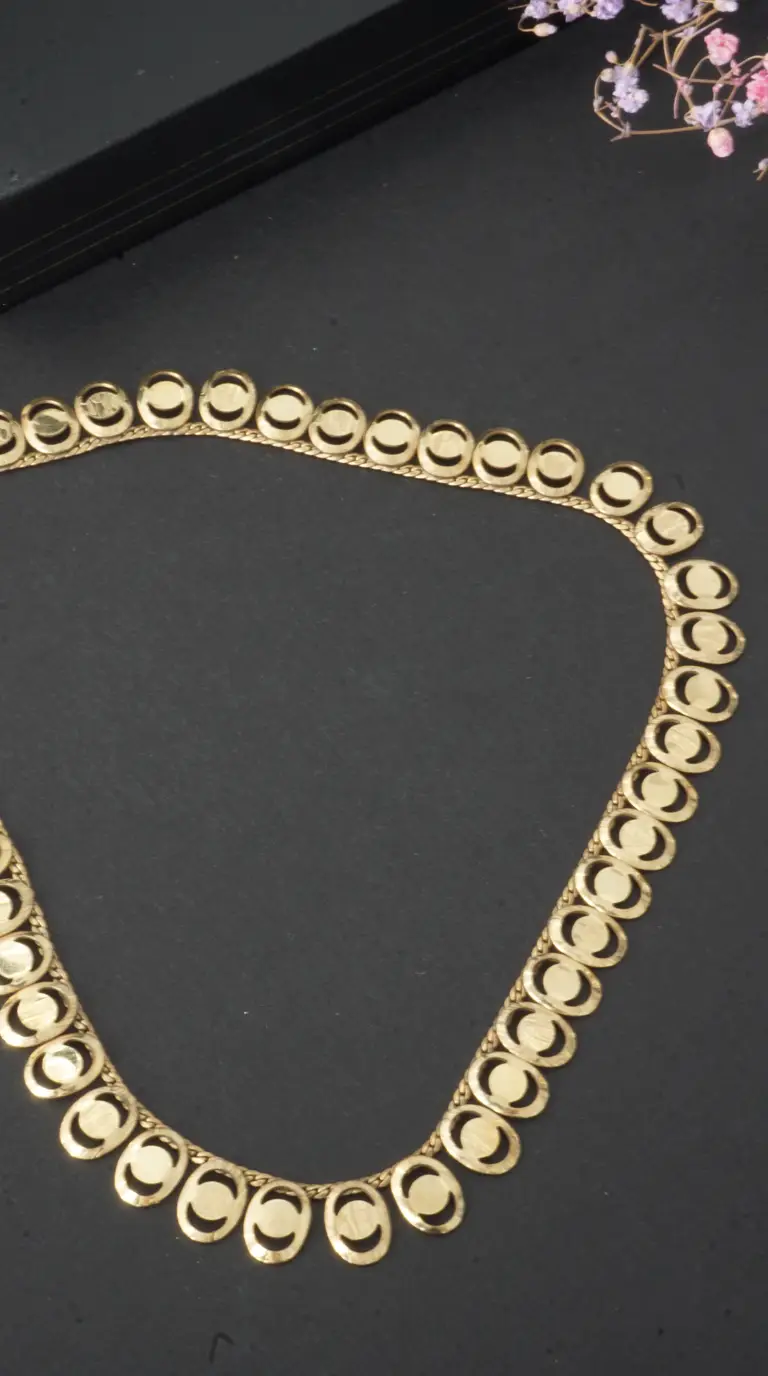 Vintage gold necklace with oval links and crescent moon cutouts on a dark background.