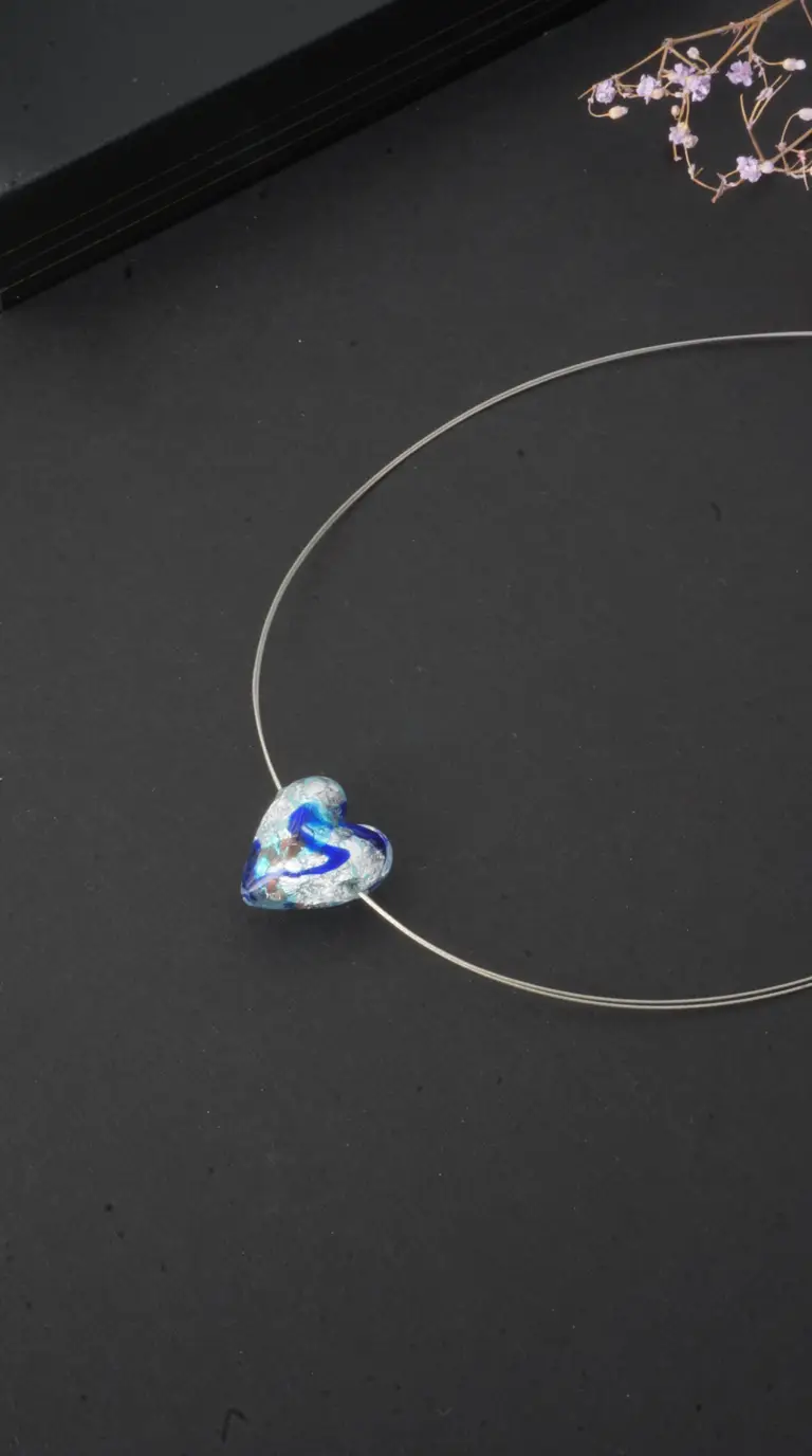 Vintage blue glass heart pendant necklace with silver swirls on a silver wire.