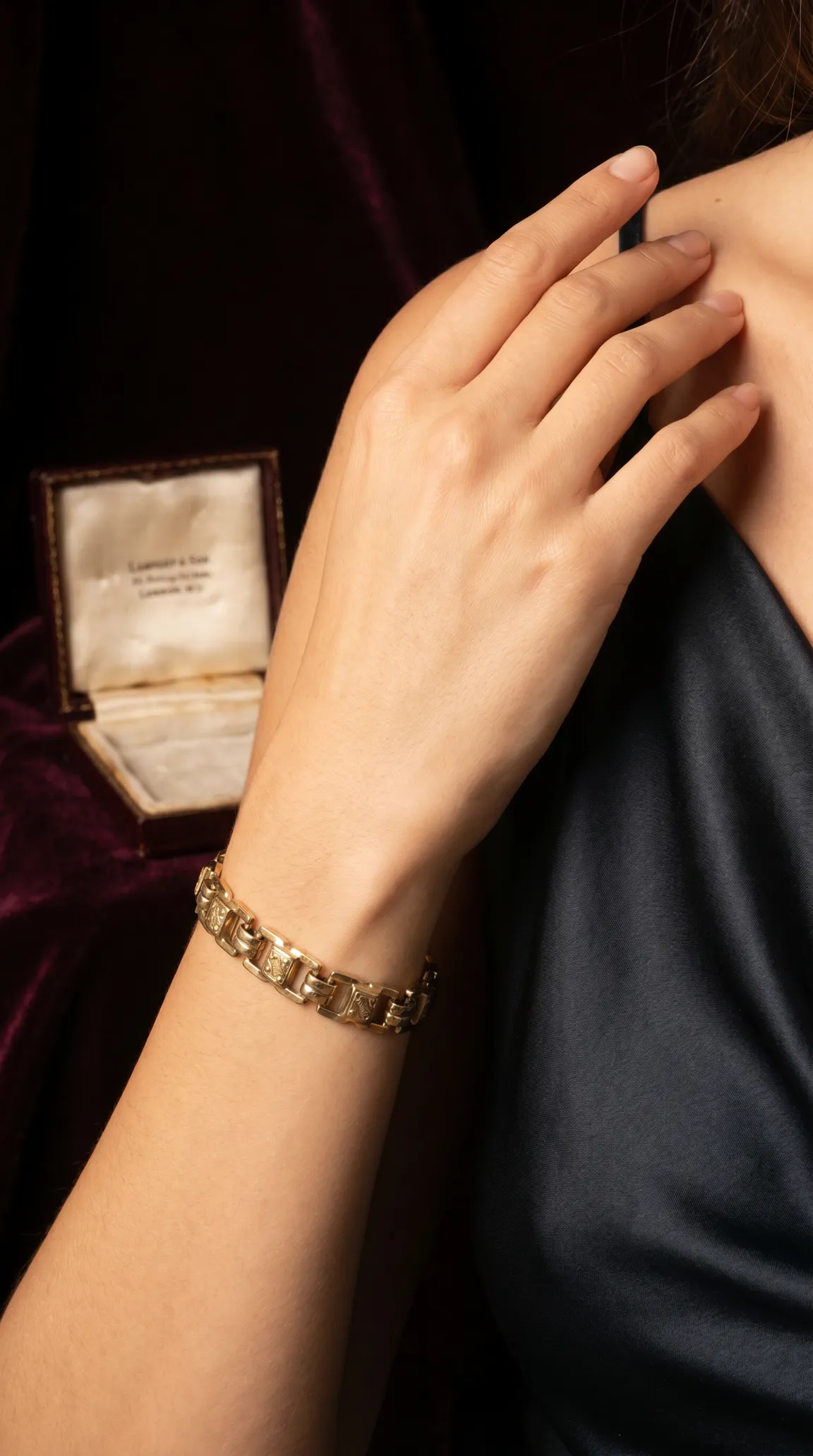 Vintage gold link bracelet with engraved detail on woman's arm, antique velvet jewelry box in background.